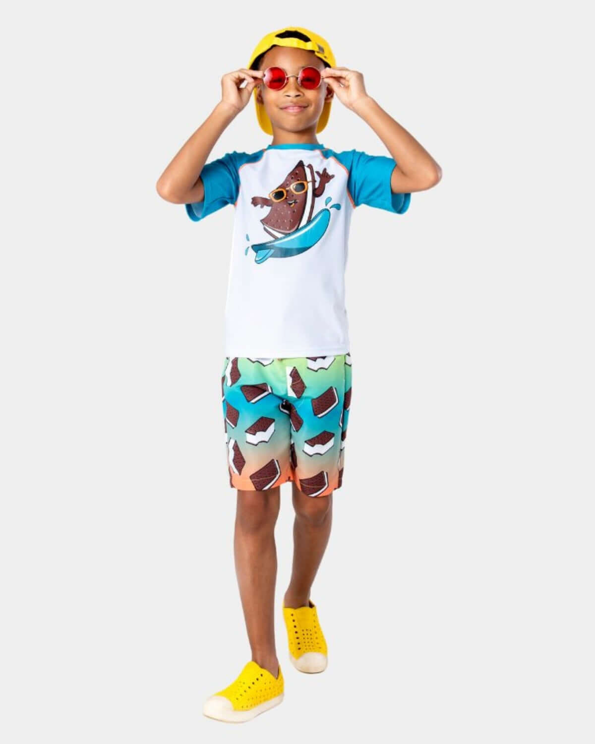 Child wearing an Ice Cream Sandwich Rash Guard and colorful swim trunks, ready for beach fun.