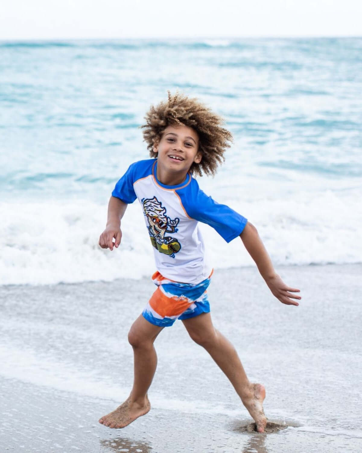 A joyful boy runs along the beach in colorful swim trunks and a playful tee, ready for sunny adventures!