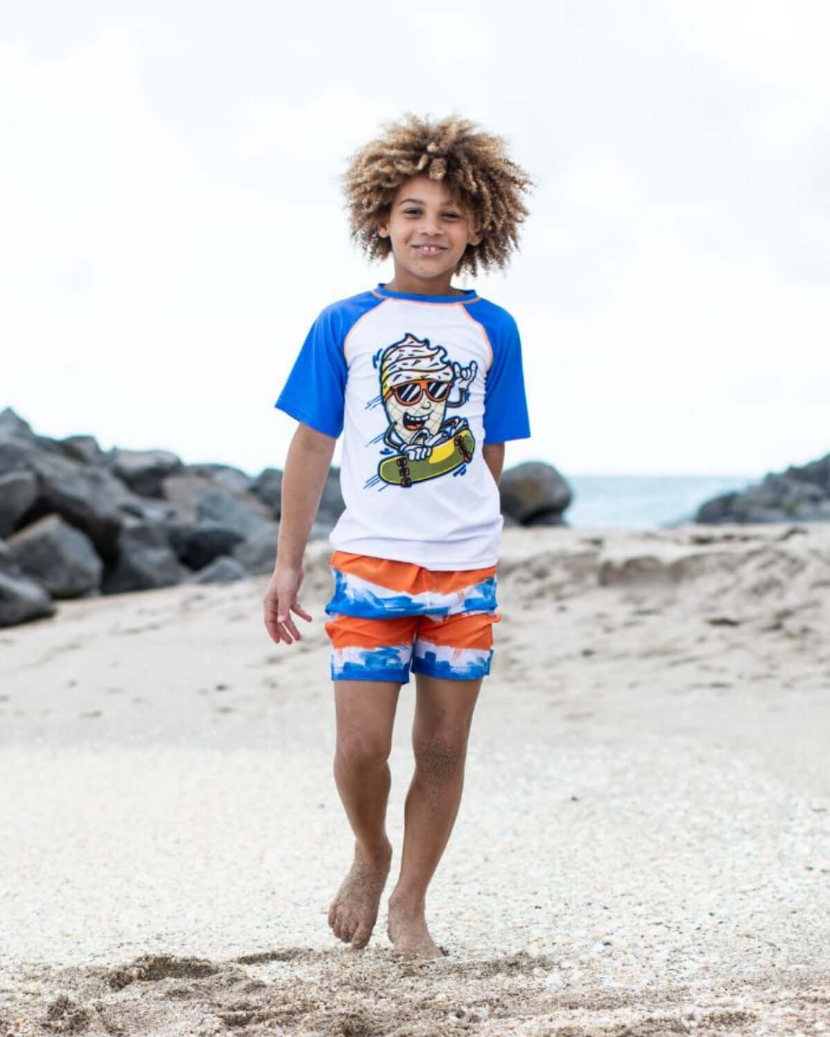 A joyful boy in Painter's Stripe Swim Trunks, ready for fun beach adventures, showcasing stylish and durable kids clothes.