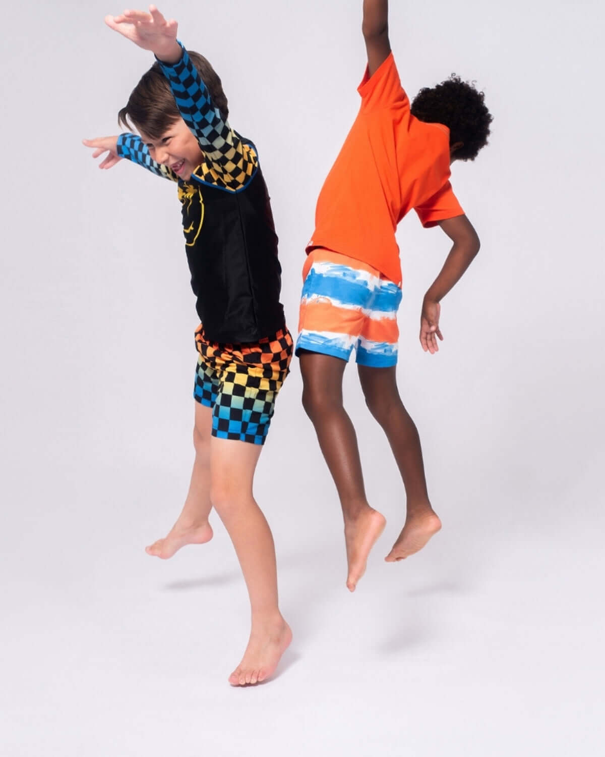 Kids in playful poses wearing Painter's Stripe Swim Trunks and vibrant swim shirts, perfect for summer fun.
