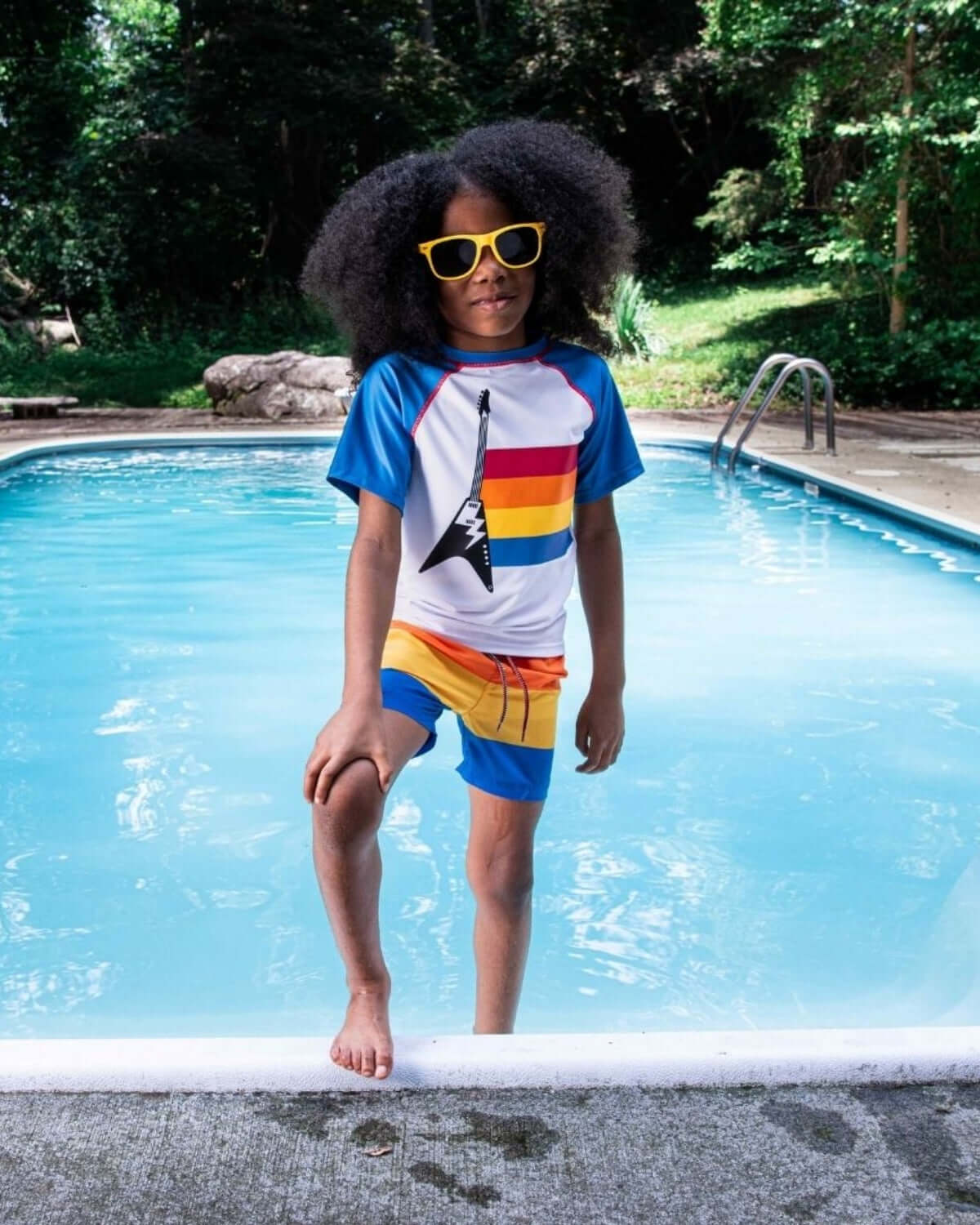 Stylish kid in retro-striped swim trunks, rocking cool sunglasses by the pool—perfect for summer fun and back to school vibes!