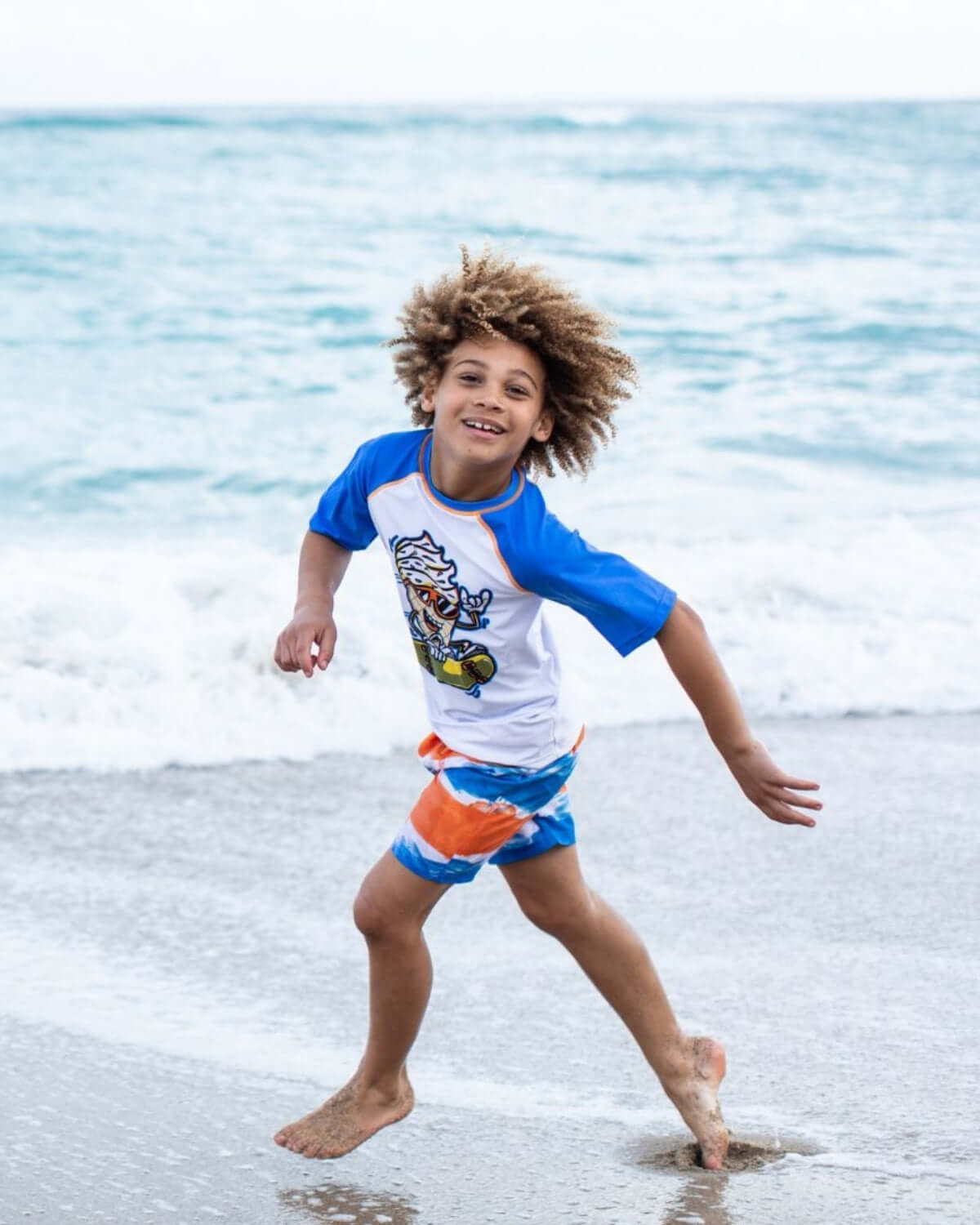 A boy wearing a Soft Served Rash Guard playing on the beach, showcasing style and comfort with sun protection.