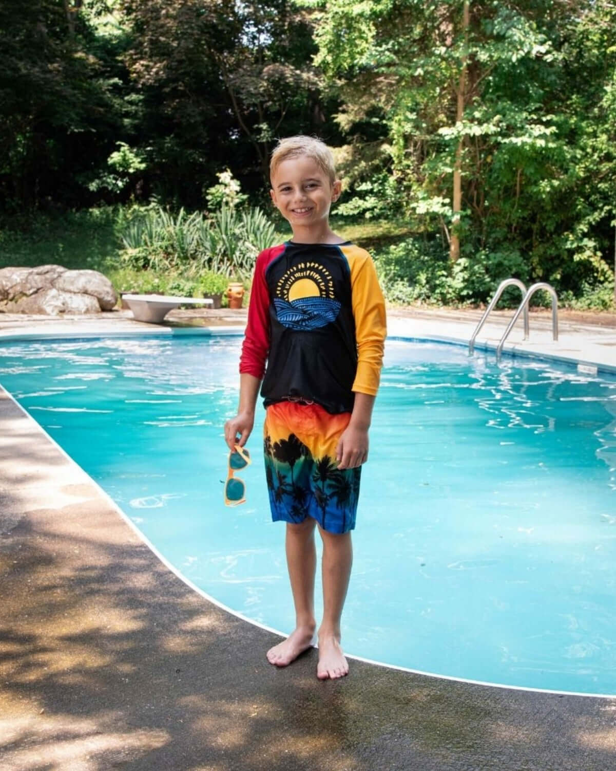 Boy wearing Sunny Waves Rash Guard and beach shorts by a poolside, ready for summer fun.
