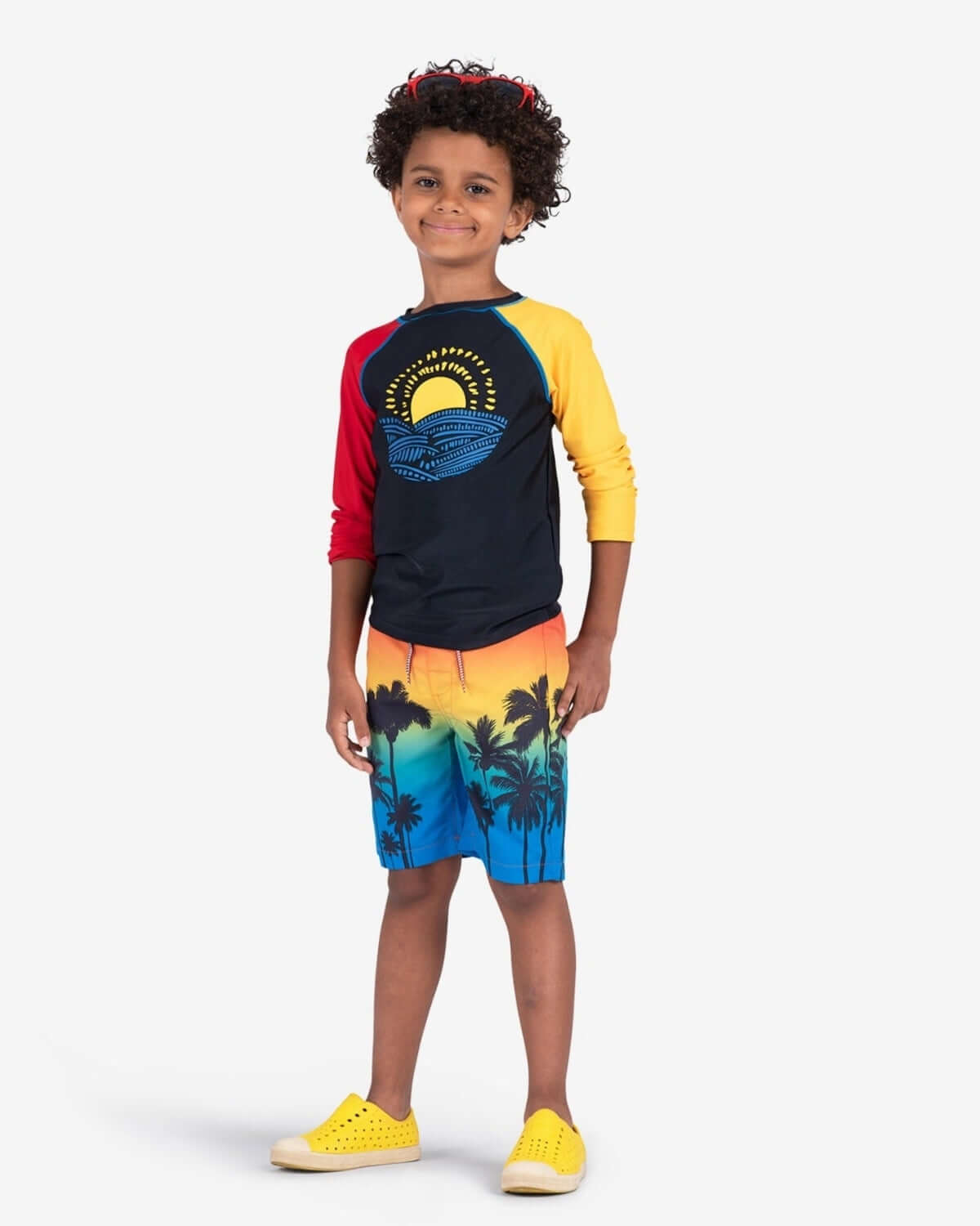 Child wearing Sunny Waves Rash Guard with colorful design, ready for summer fun at the beach.
