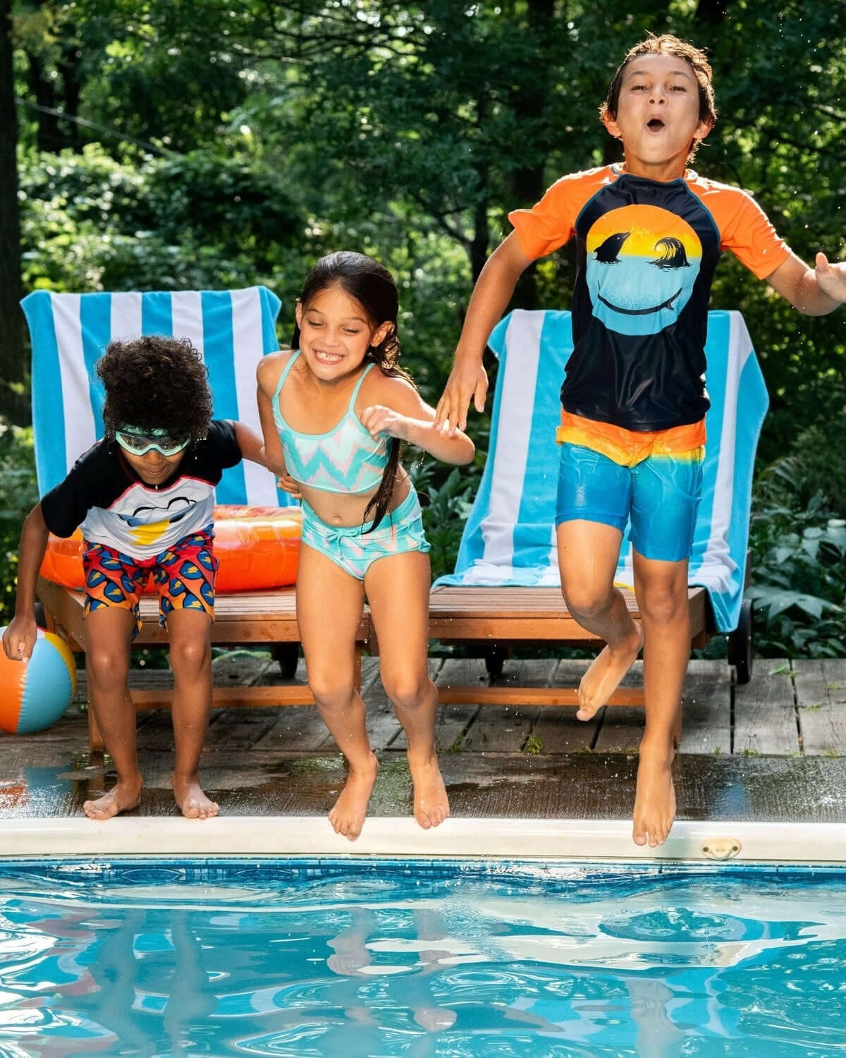 Three kids in vibrant swim trunks joyfully jumping into a pool, showcasing fun, stylish kids clothes for summer adventures!