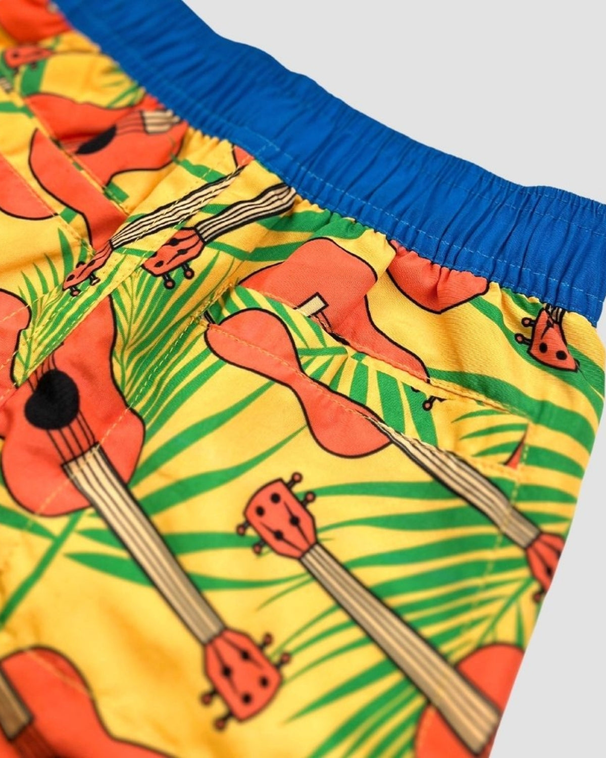 Vibrant ukulele-patterned swim trunks with a blue waistband—perfect for stylish kids' beach days!