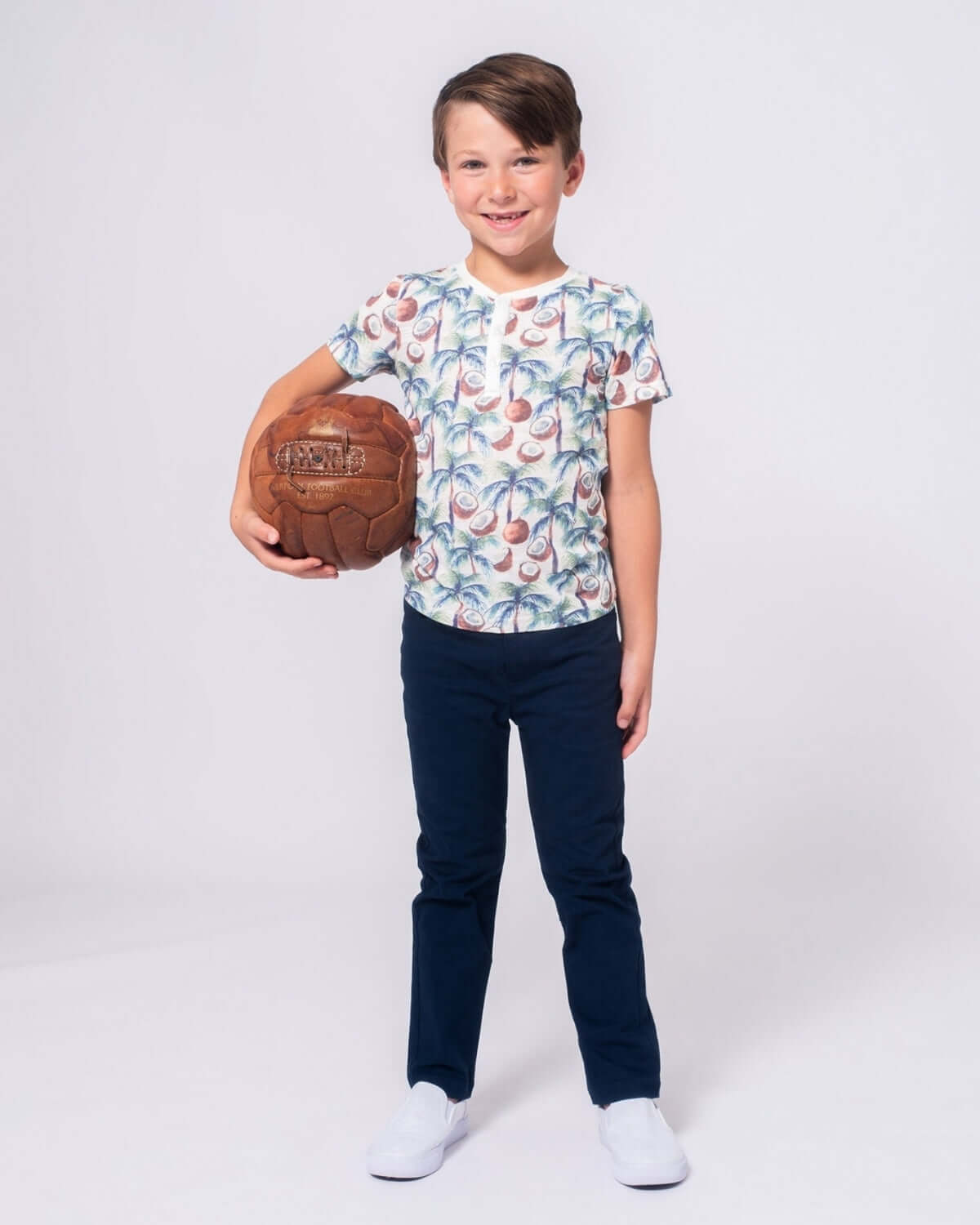 Playful boy in coconut palms Henley shirt, ready for fun with a soccer ball—stylish kids clothes for adventures!