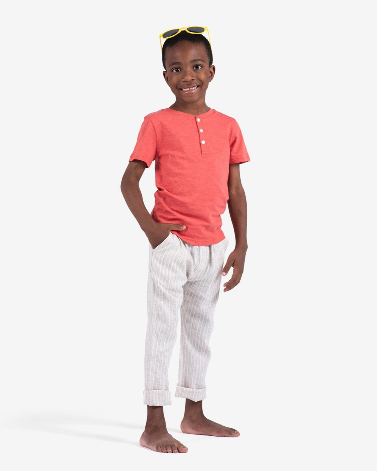 Stylish boy in coral Day Party Henley shirt, rocking relaxed striped pants for a fun summer look in kids clothes.