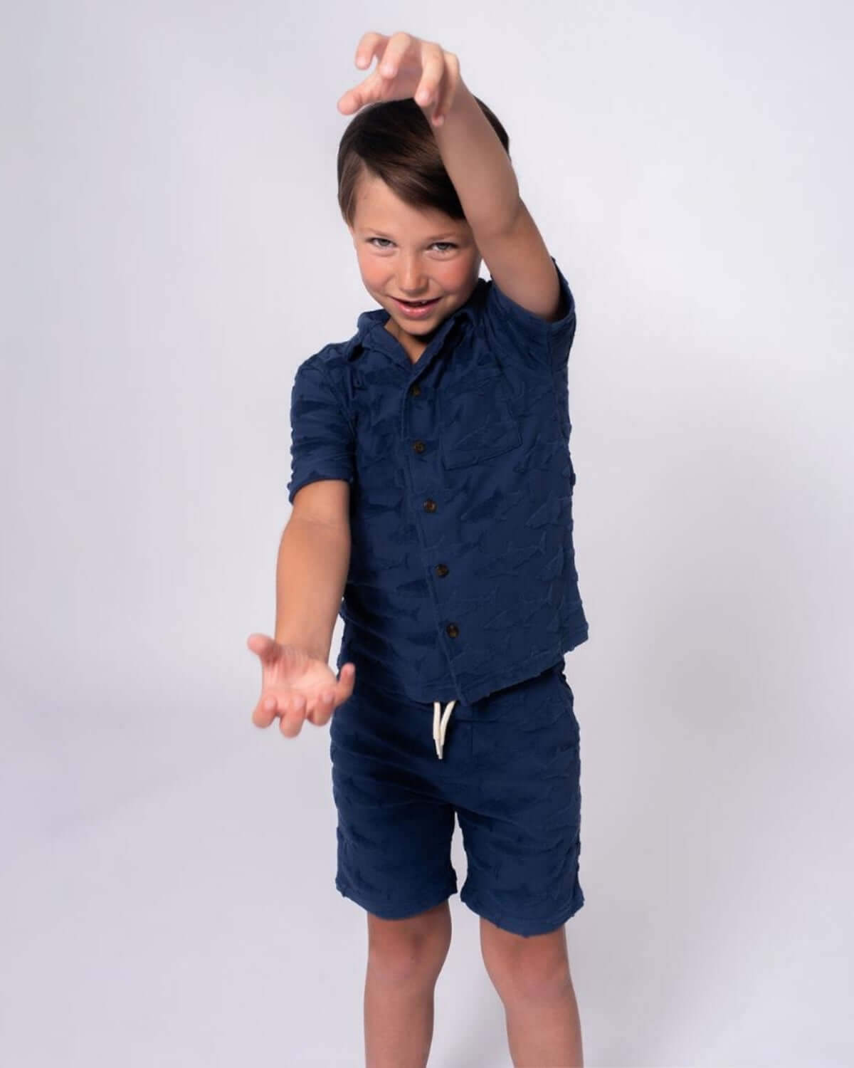 Boy in Navy Shark Resort Terry Shirt and shorts poses for the camera, showcasing fun ocean-inspired style.