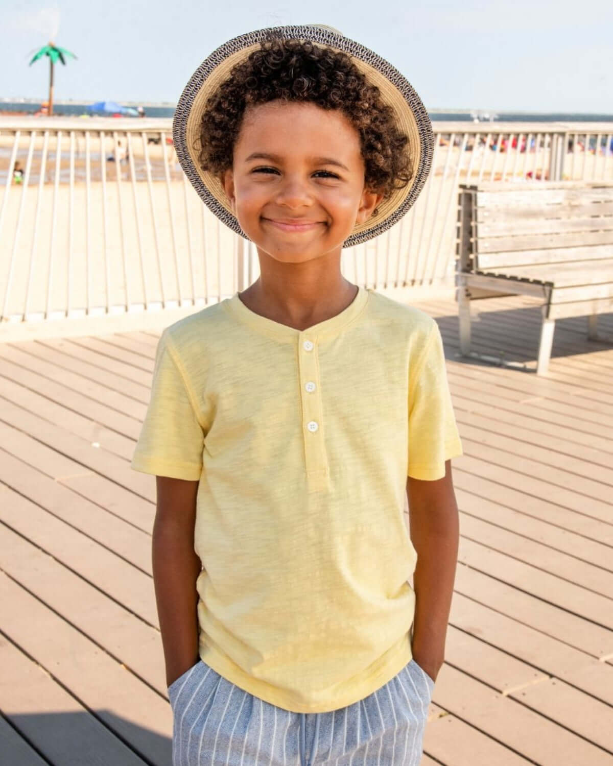 Pale Yellow Day Party Henley worn by a smiling boy at the beach, showcasing a casual summer style.