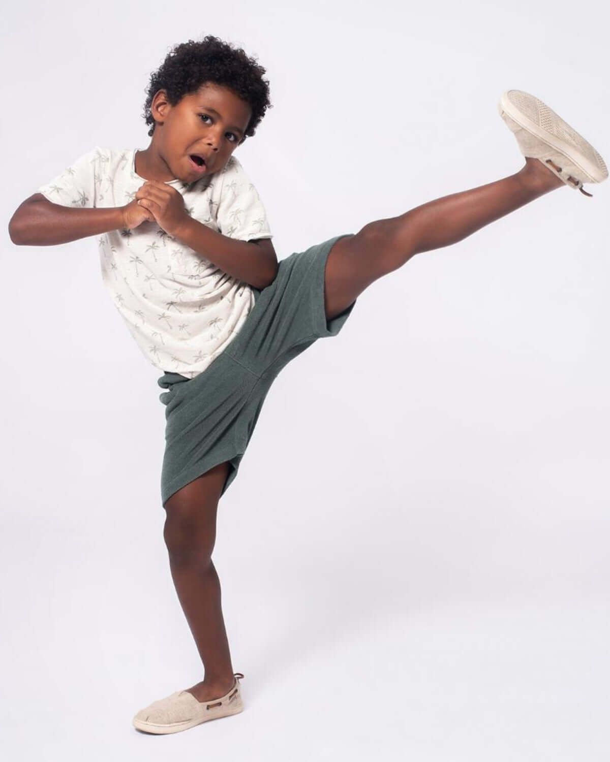Joyful boy kicking in stylish palm tree tee and comfy shorts, showcasing quality kids clothes for active play and summer fun.
