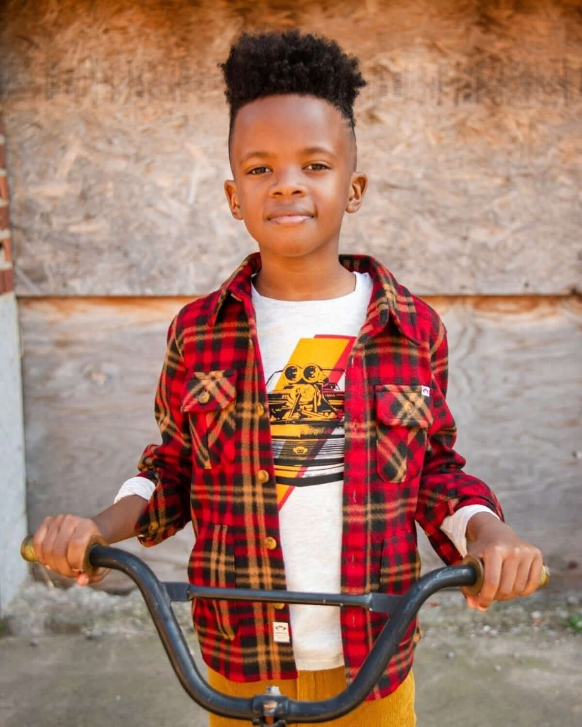 Boy wearing a Rio Red Plaid Snow Fleece Shirt, riding a bicycle, outdoors in a warm and cozy setting.