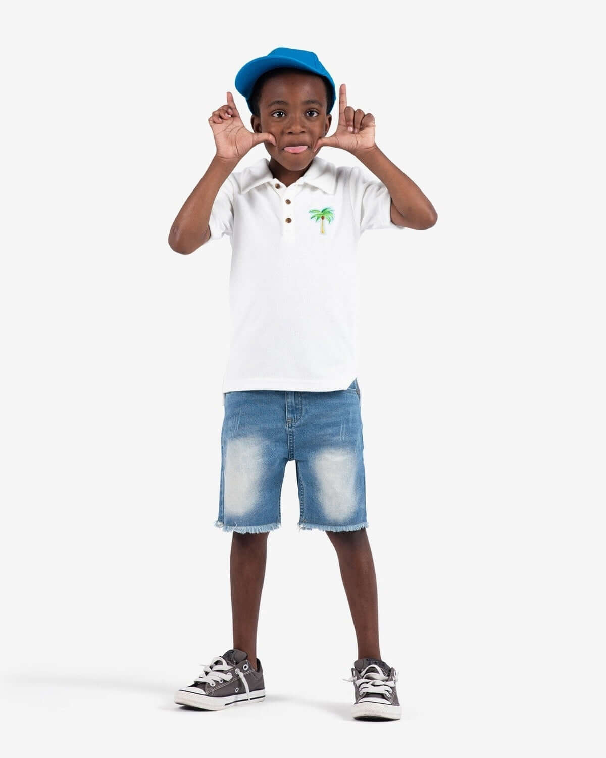 Stylish boy in a white Fairbanks polo with palm tree embroidery, sportin' a playful pose—perfect for back to school adventures!