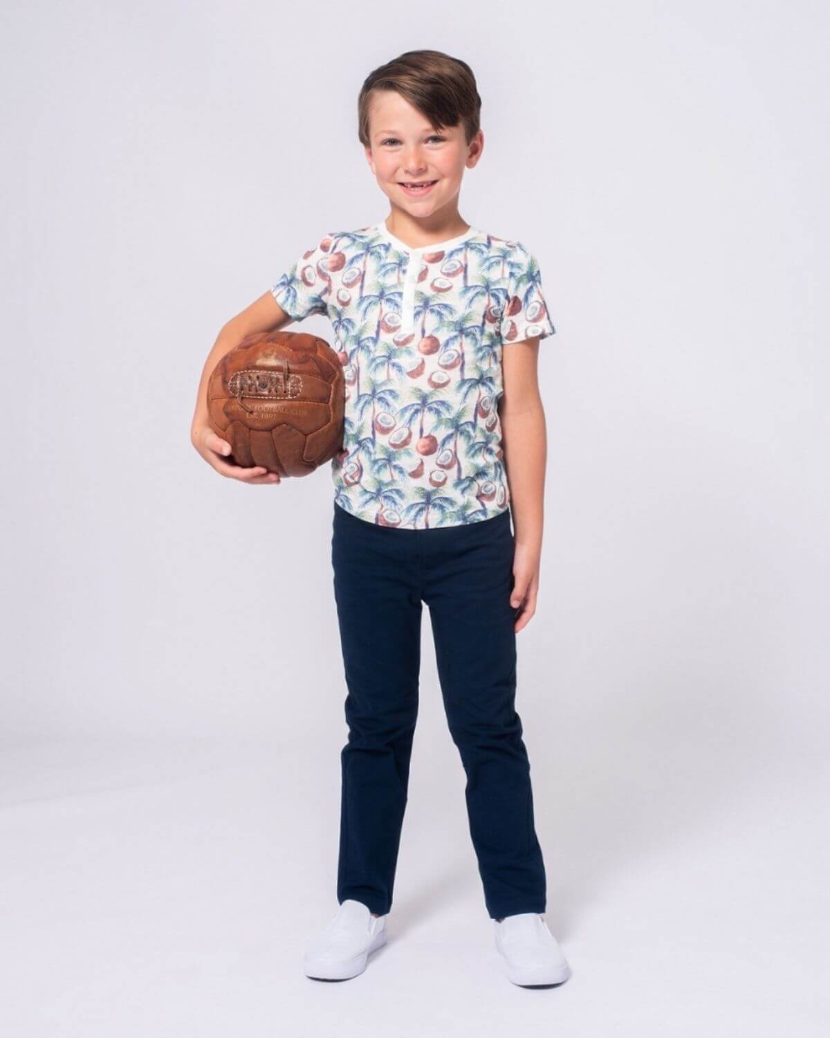 Stylish kid in playful floral tee and navy pants, ready for adventure with his soccer ball! Perfect kids clothes for back to school.