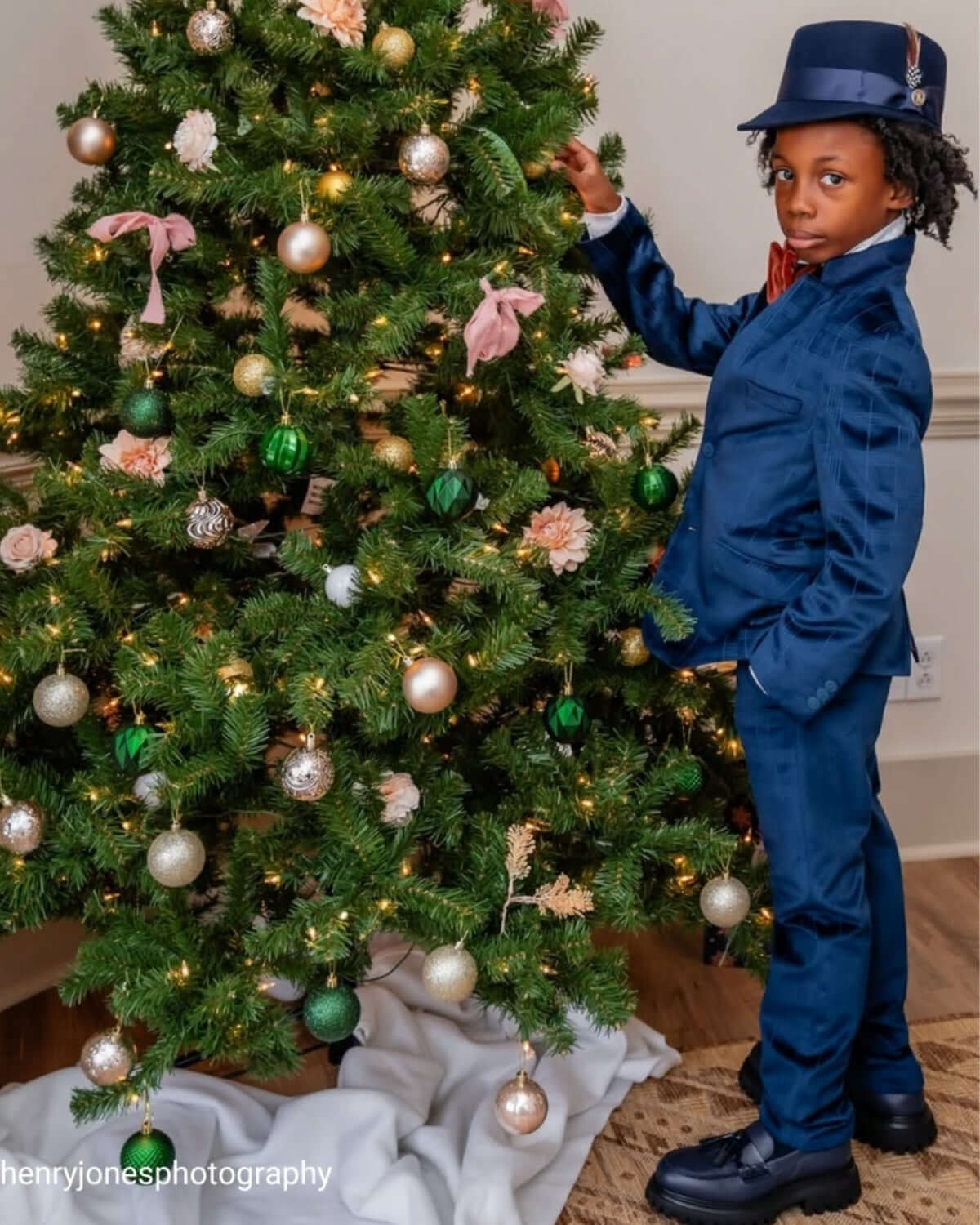 Stylish kid in a navy suit posing by a festive Christmas tree, capturing holiday cheer with confidence and flair.