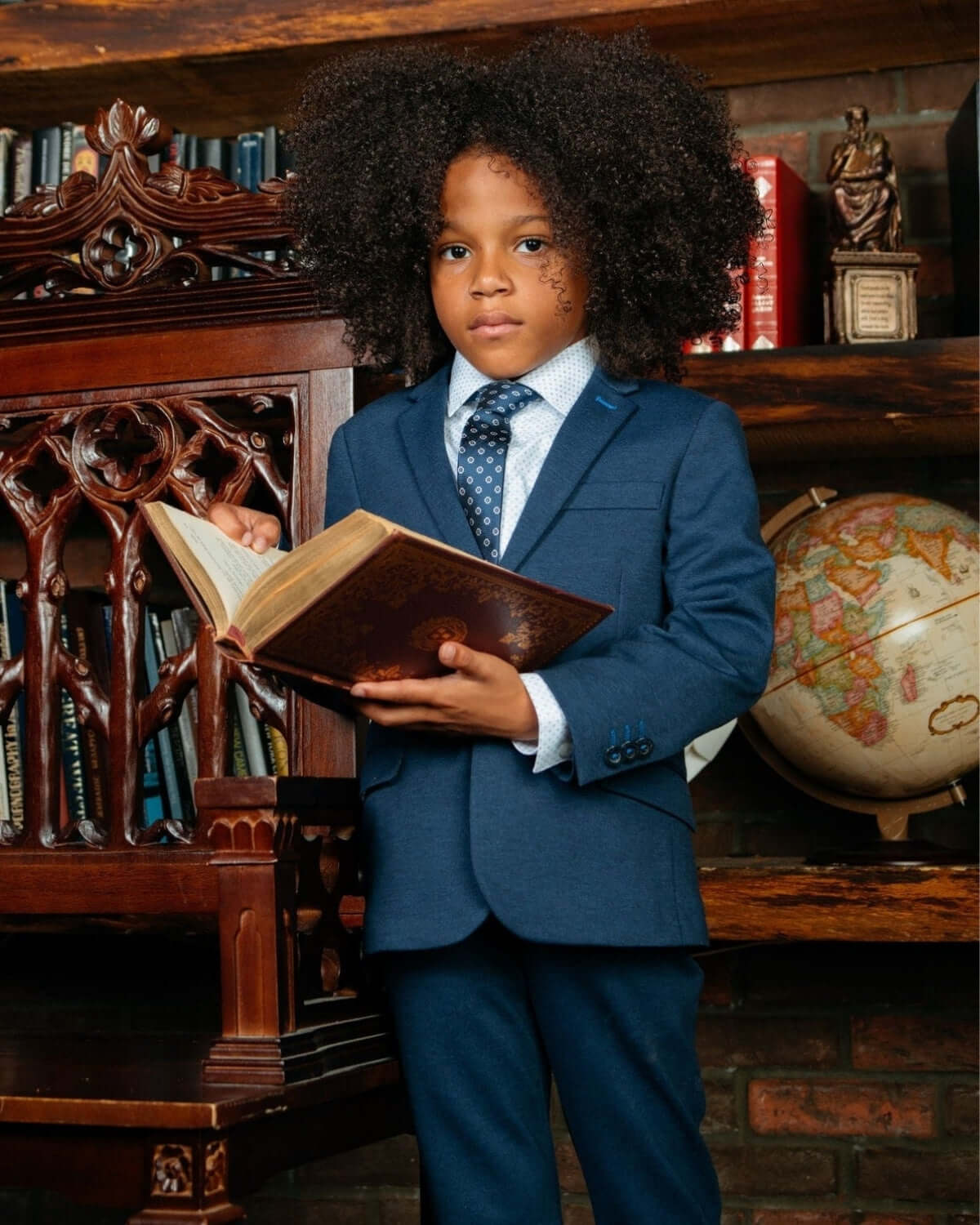Stylish boy in a blue suit reading a book, exuding confidence and charm for back-to-school season in high-quality kids clothes.