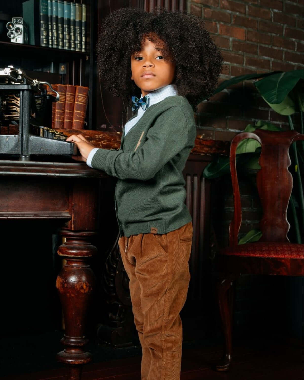 Stylish boy in a green cardigan and corduroy pants at a vintage desk—perfect for back-to-school adventures!