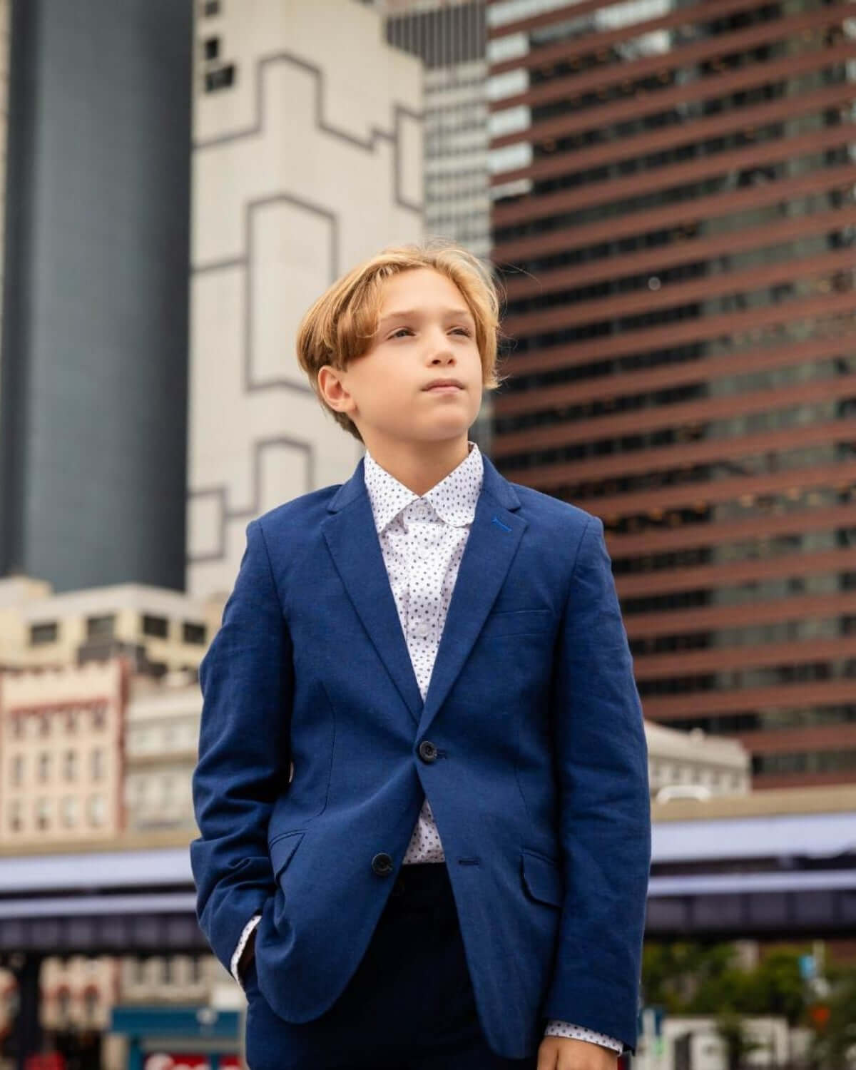 Stylish boy in estate blue suit exuding confidence against a modern city backdrop—ideal for kids' high-quality clothes!