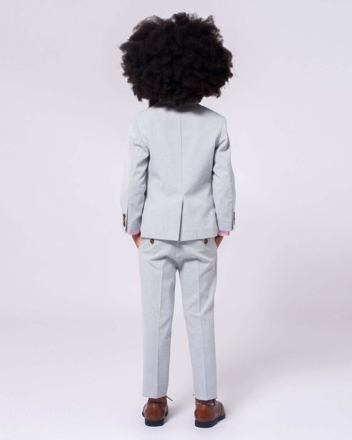 A stylish kiddo showing off the back of high rise grey stretchy suit pants—modern fashion for little gentlemen!