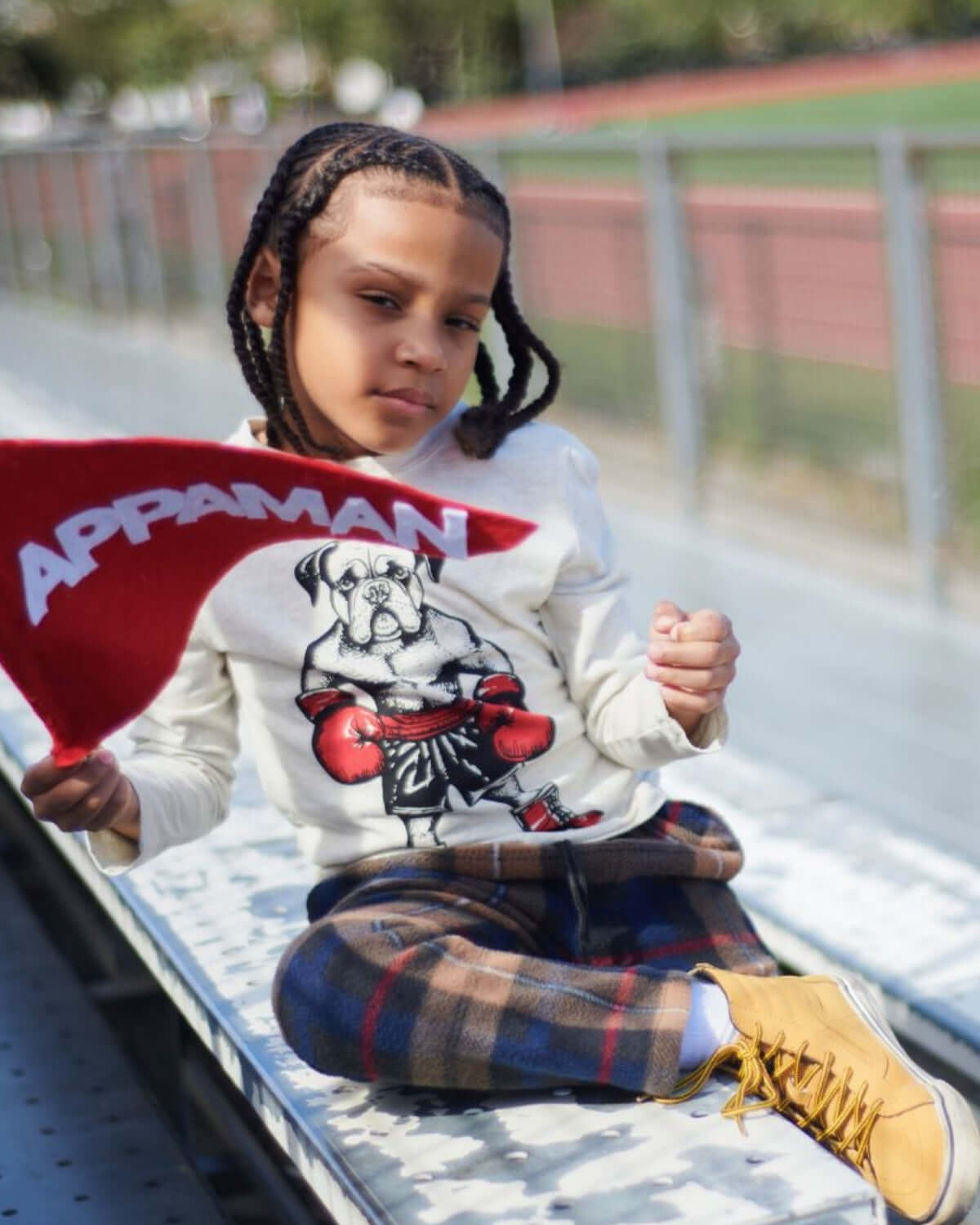Stylish kid rocking Appaman's plaid club pants and a playful dog graphic tee, showing off school spirit with a flag.