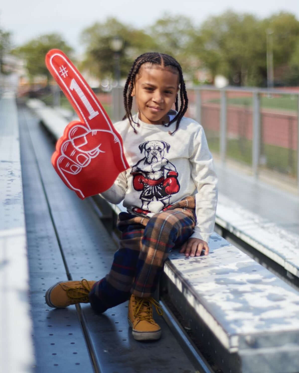 Stylish boy proudly holding a #1 foam finger, dressed in fun plaid pants and a playful dog print shirt, ready for game day!