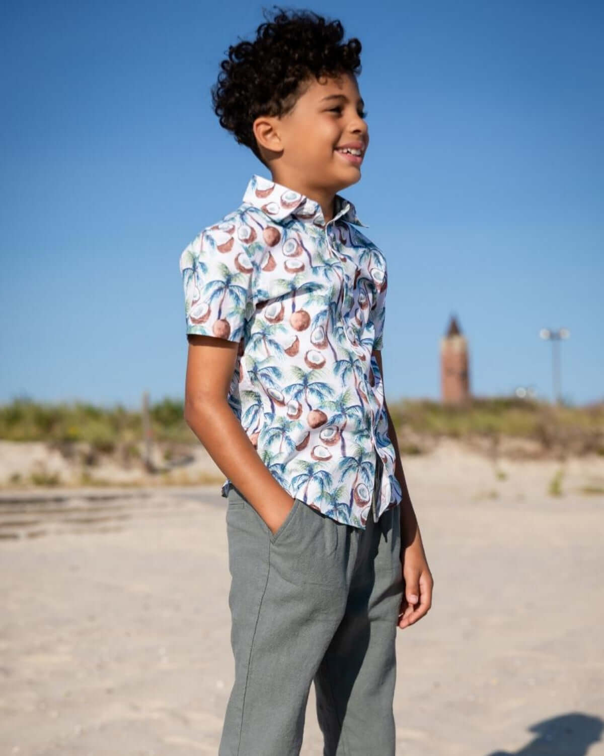 Stylish boy wearing a playful palm-print shirt and comfy pants, ready for beach fun and sunny adventures in kids clothes.