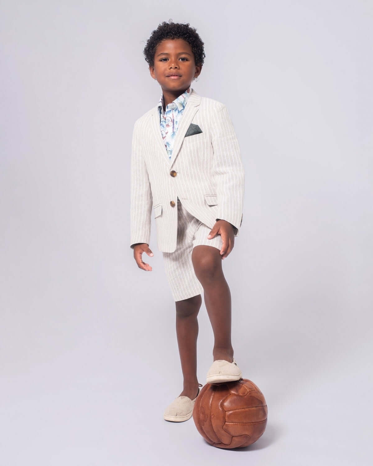 Chic boy in sand stripe trouser shorts and blazer, poised on a soccer ball, ready for summer fun and stylish adventures!
