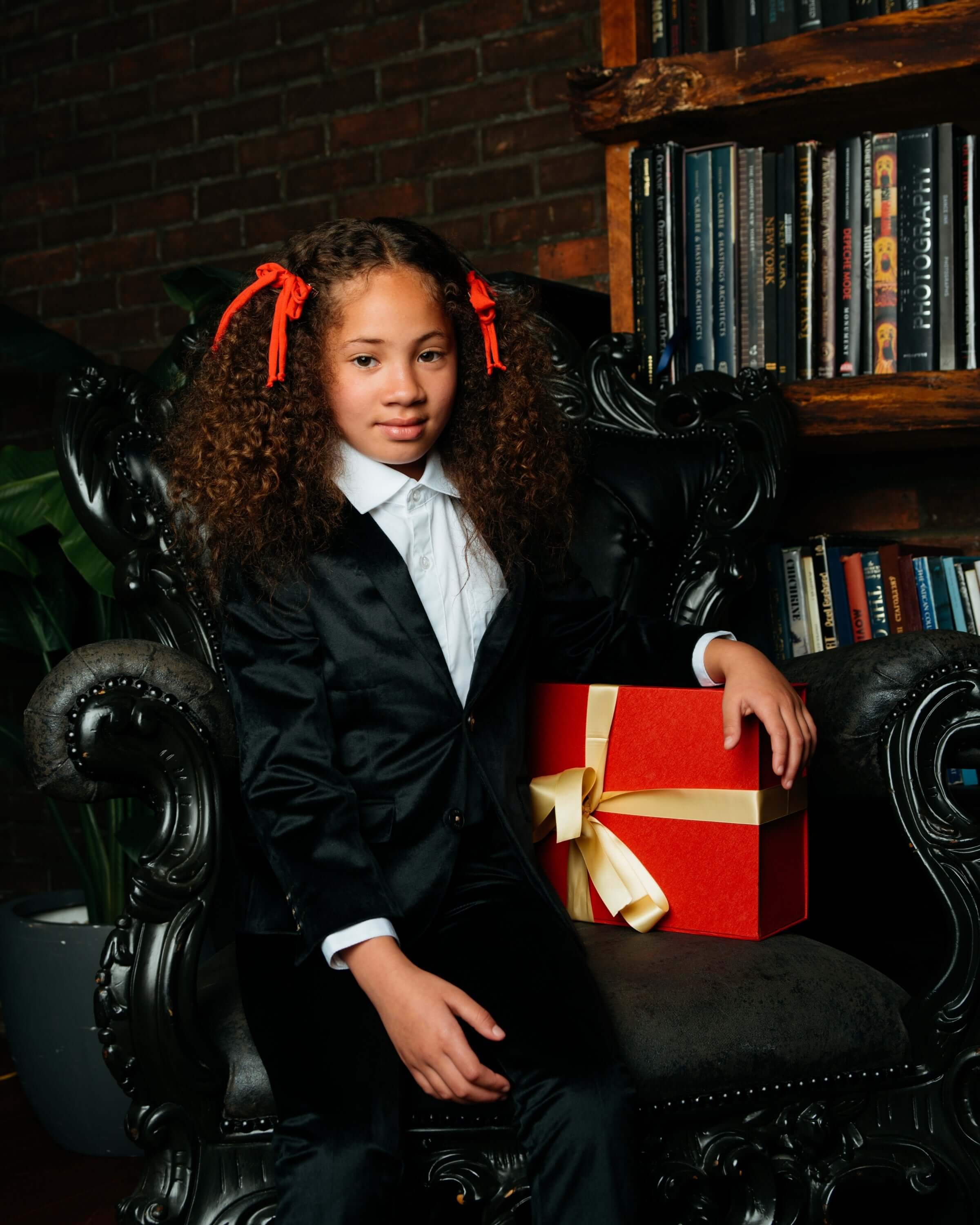 Stylish girl in a black velvet blazer with a red gift, radiating holiday cheer and confidence.