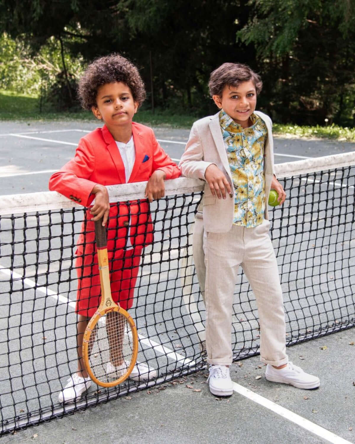 Two stylish boys in vibrant coral and neutral suits, ready to ace playtime with charm and confidence on the tennis court.