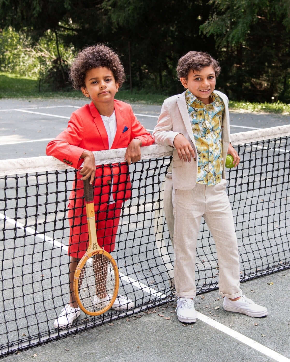 Two stylish boys in colorful suits by the tennis court, perfect for chic kids clothes this back to school season.