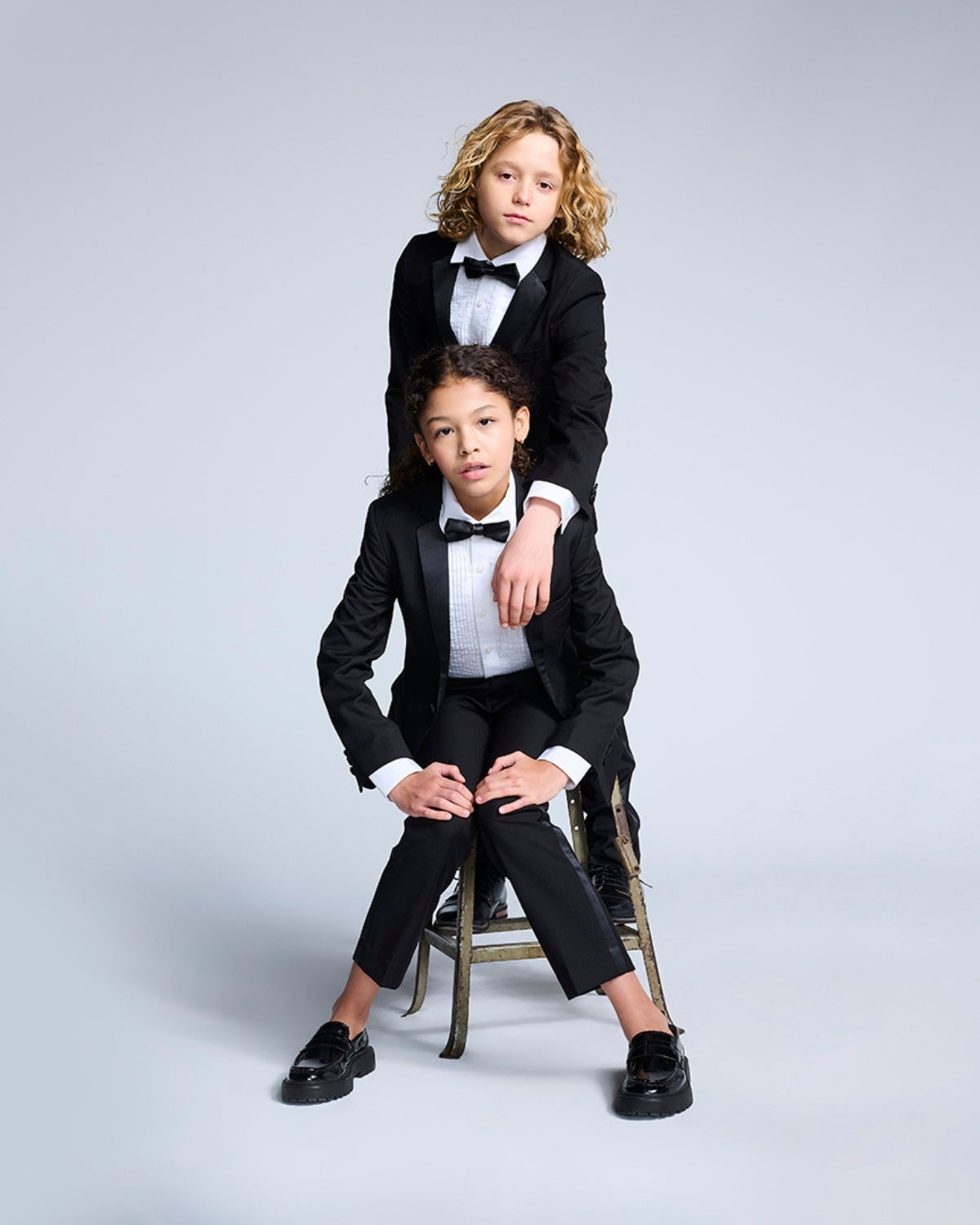 Two stylish kids rocking tuxedo pants and bow ties, ready to steal the spotlight at any black tie affair.