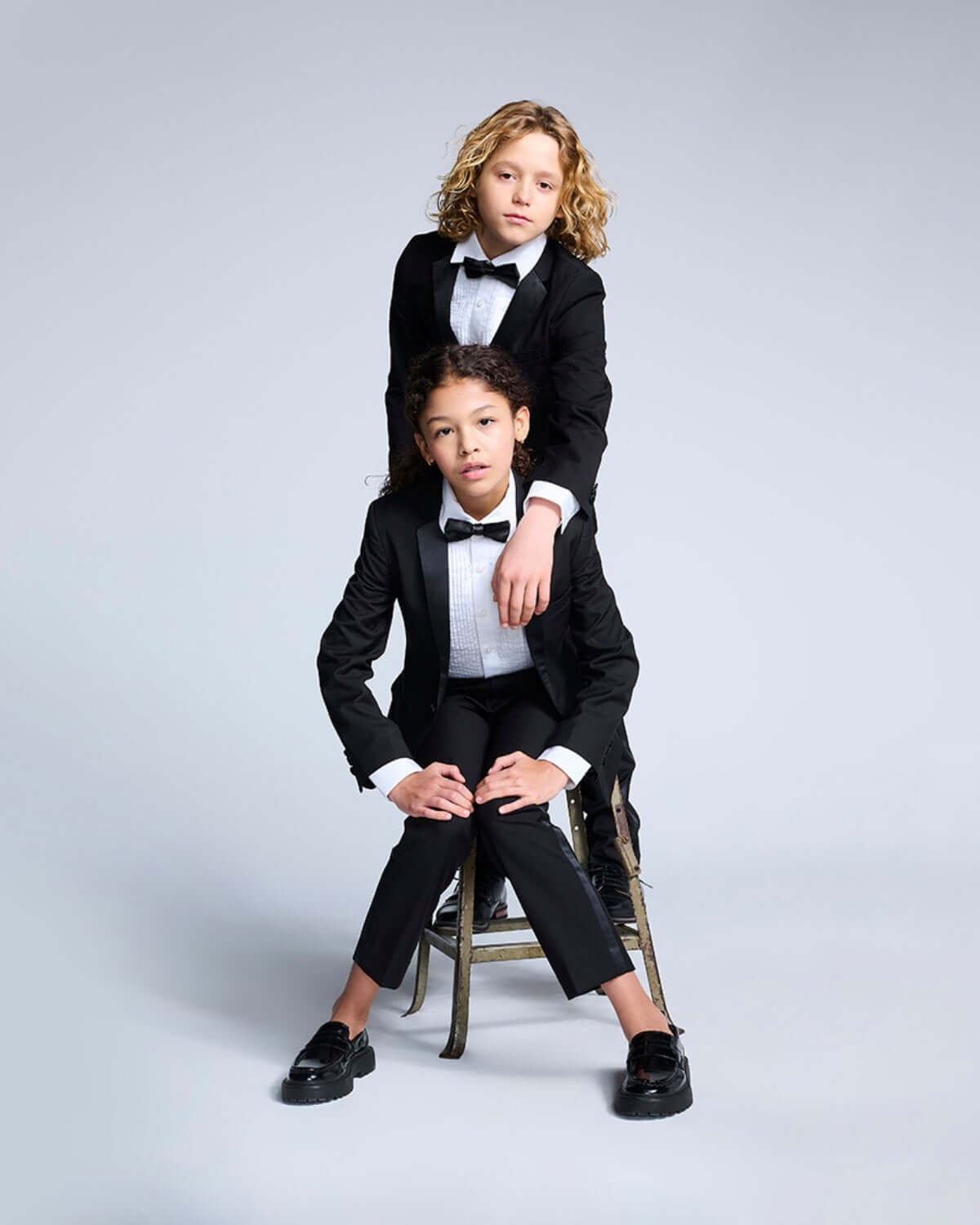 Two kids wearing Black Tuxedo Pants and bow ties, posing elegantly in a stylish formal attire.