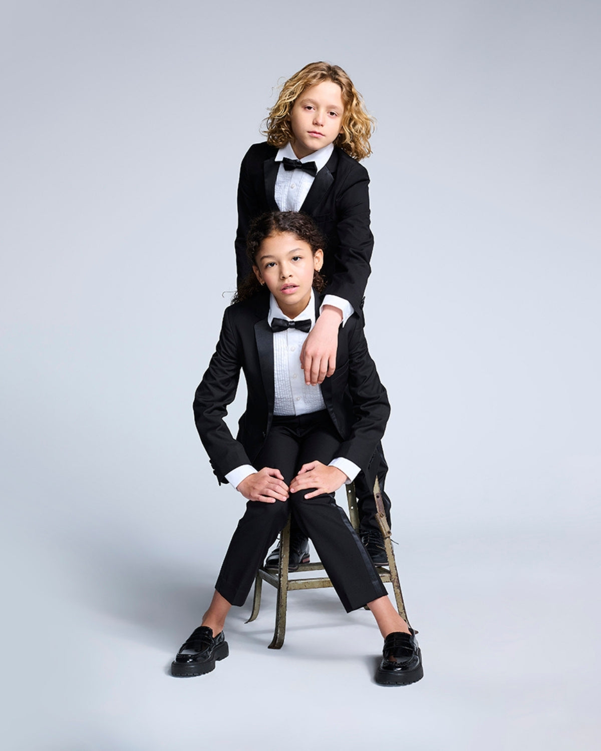 Two stylish kids in sleek black tuxedos, ready to steal the spotlight at any formal event! Perfect for little trendsetters.