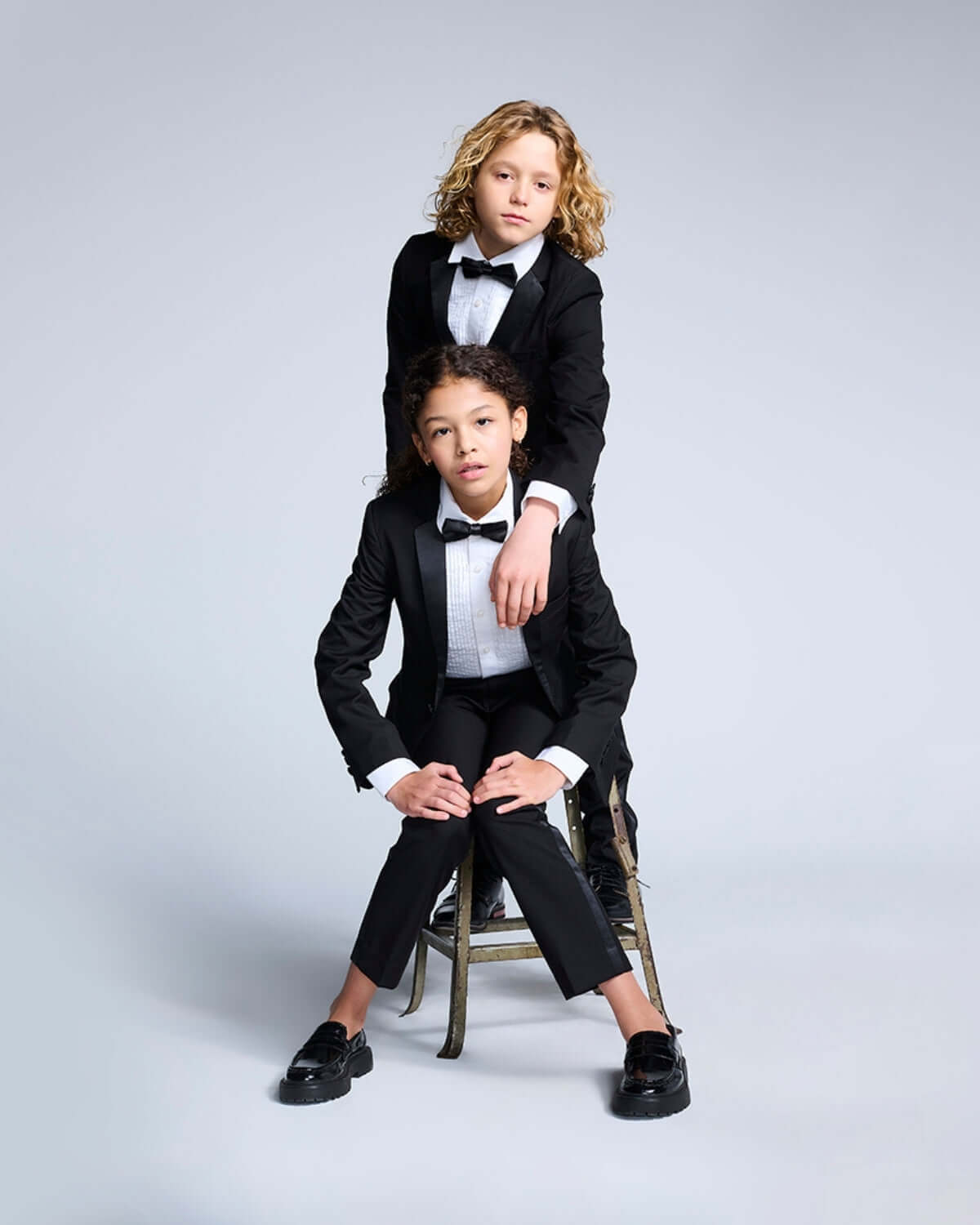 Two children wearing a Black Tuxedo Suit Jacket and bow ties, posing stylishly for a formal event.