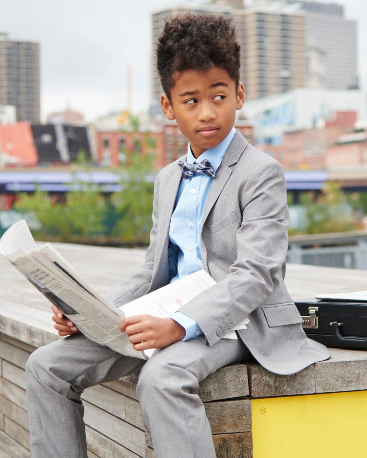 Dapper young gentleman in a grey suit, exuding charm and confidence while reading in the city—stylish kids clothes for any event.