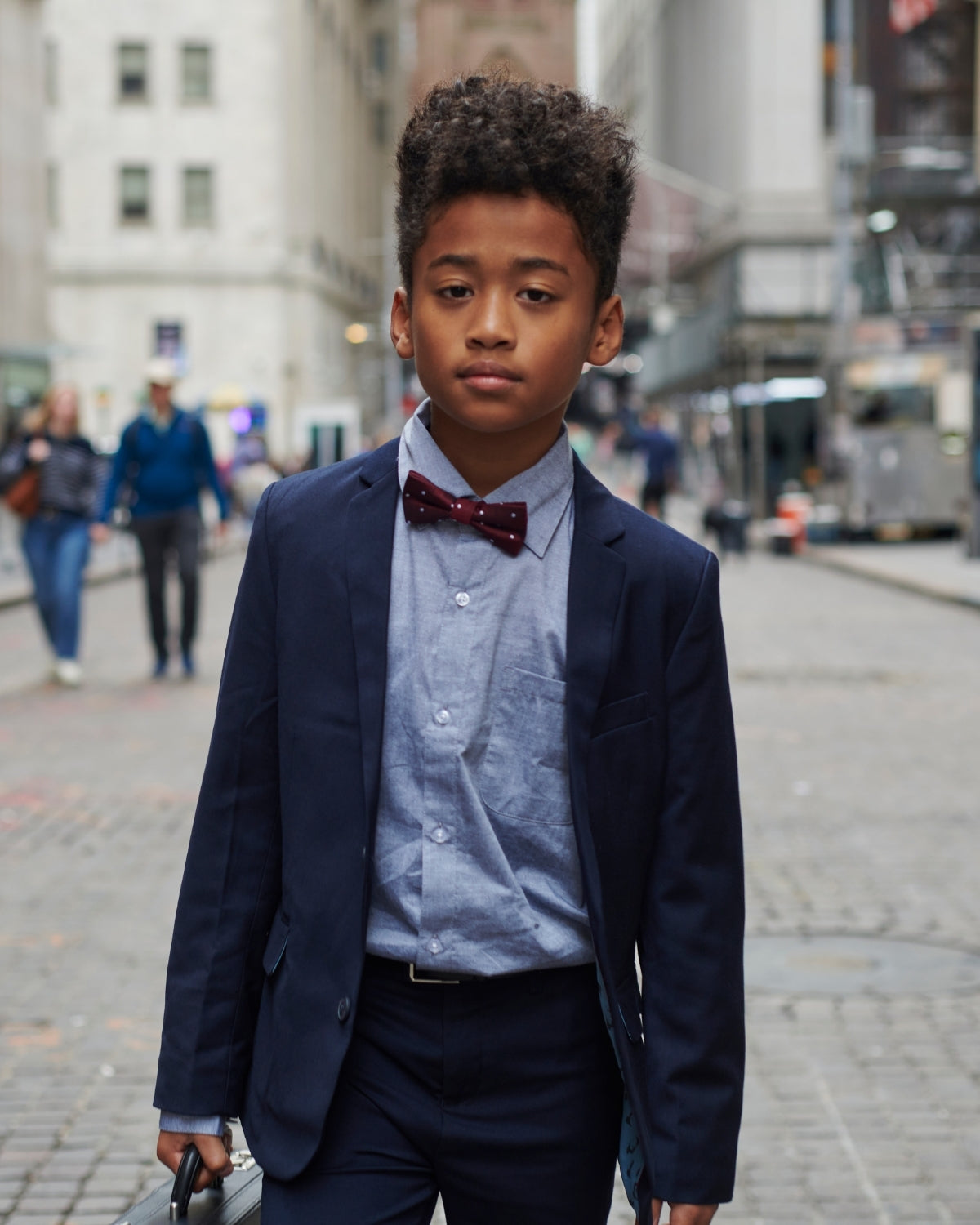 Stylish boy confidently strutting in a navy blue suit and bow tie, ready for a special event in the city.