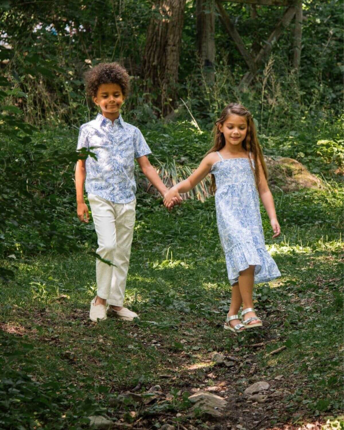 Kids wearing Blue Palms Day Party Shirt and Madison Dress in Blue Palms walking hand in hand outdoors.
