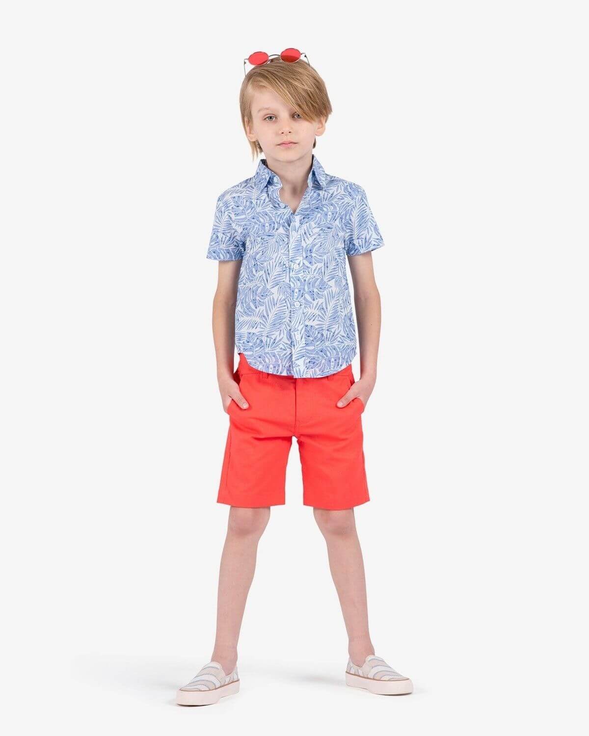 Boy wearing a Blue Palms Day Party Shirt paired with coral shorts and sunglasses.