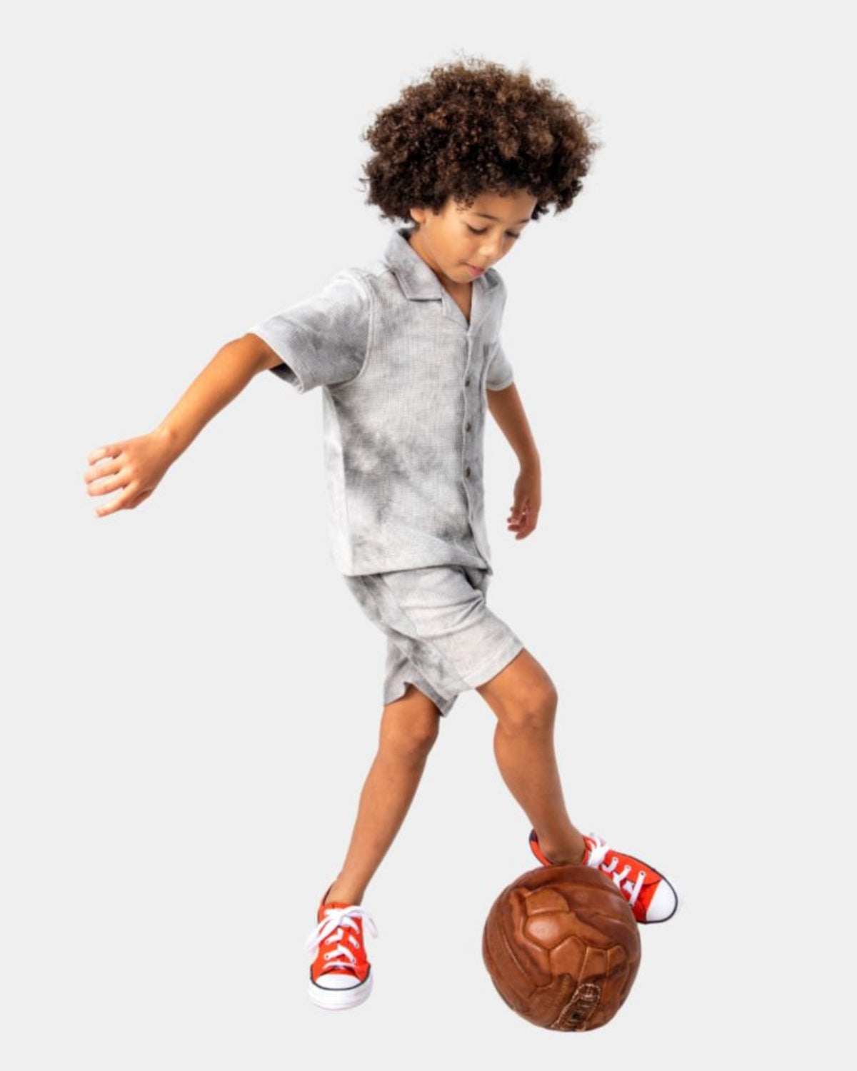 Playful kid in Grey Tie Dye Resort shirt and shorts, kicking a soccer ball with confidence and style.