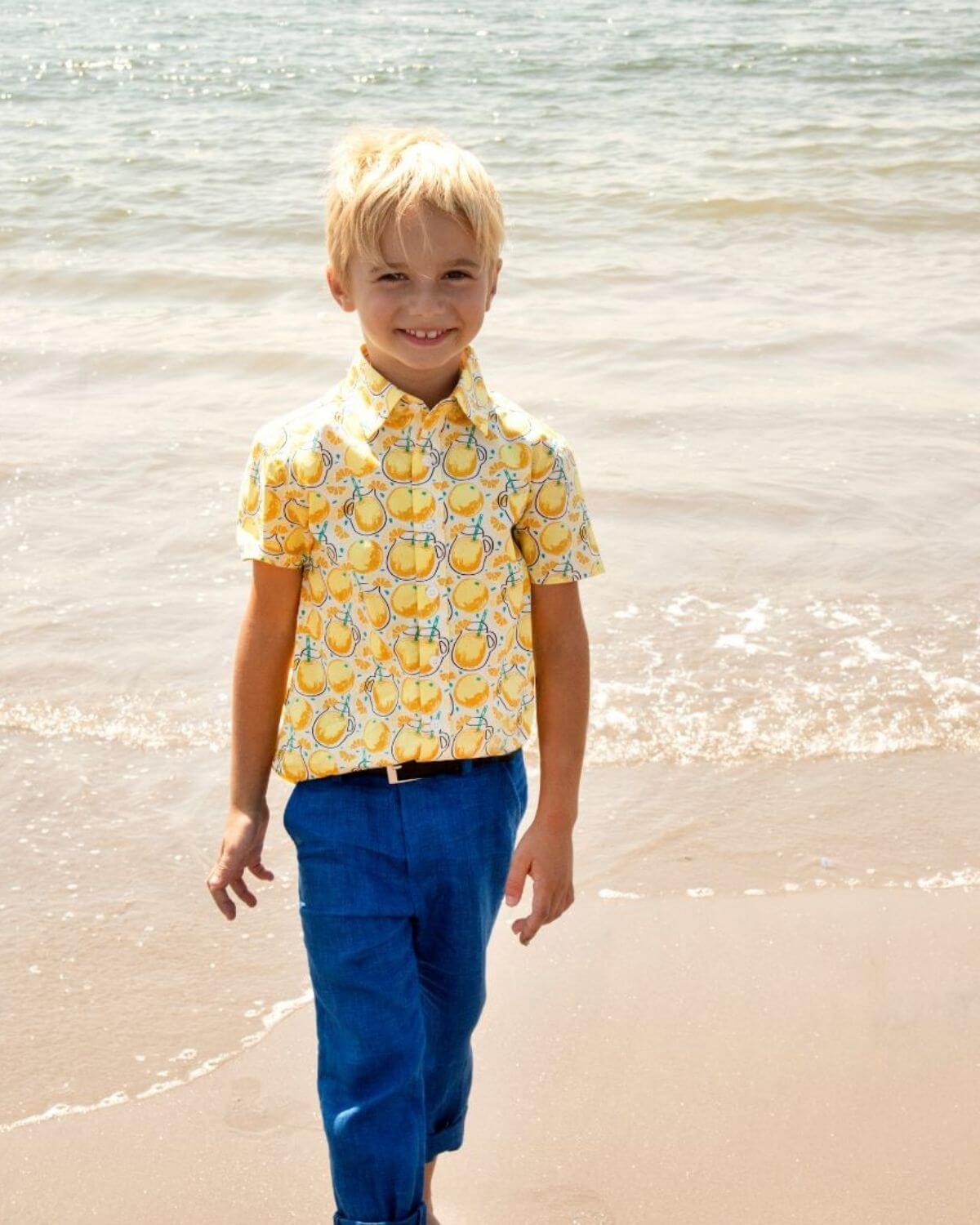 Child wearing a Lemonade Day Party Shirt with a fun lemon print at the beach, capturing summer vibes.
