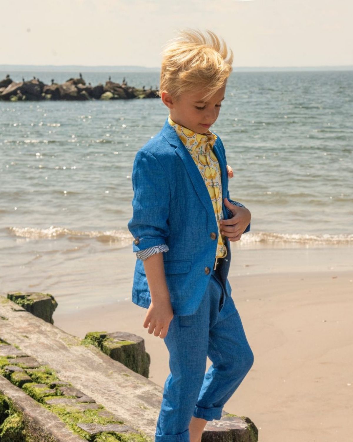 Stylish boy in a blue suit and bright shirt, enjoying a beach day—perfect kids clothes for summer fun!