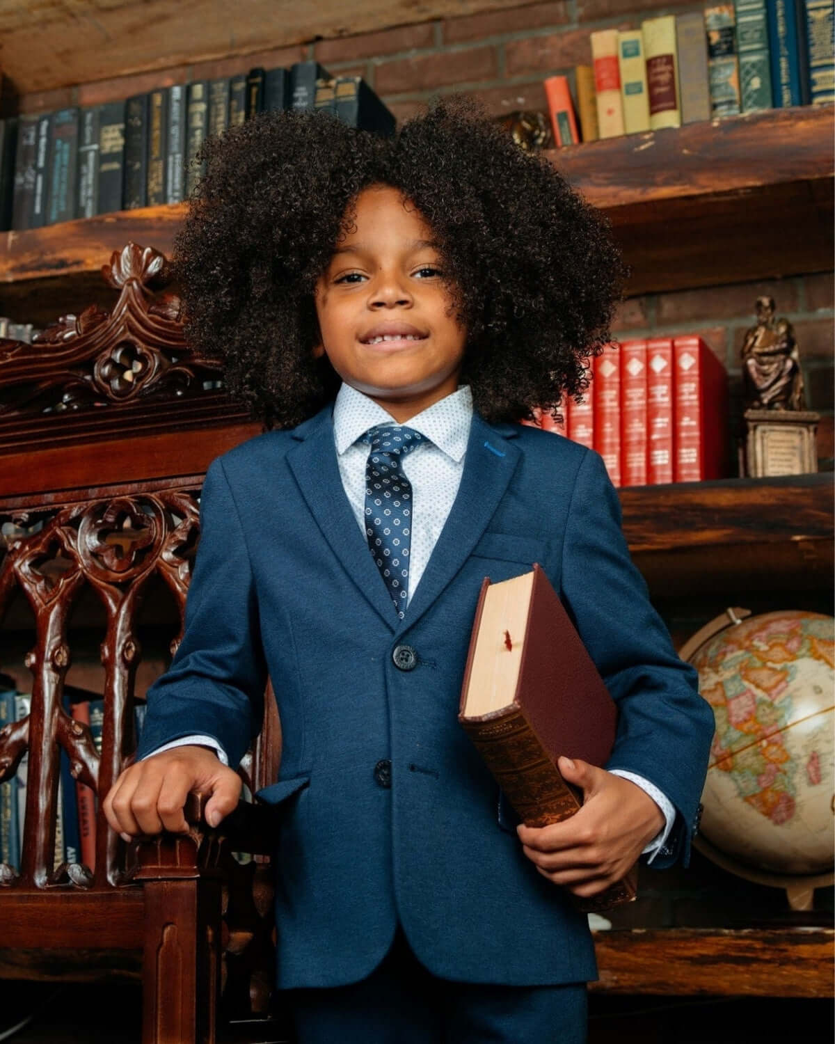 Stylish boy in a navy blue suit with a book, showcasing modern kids clothes for a sharp back-to-school look.