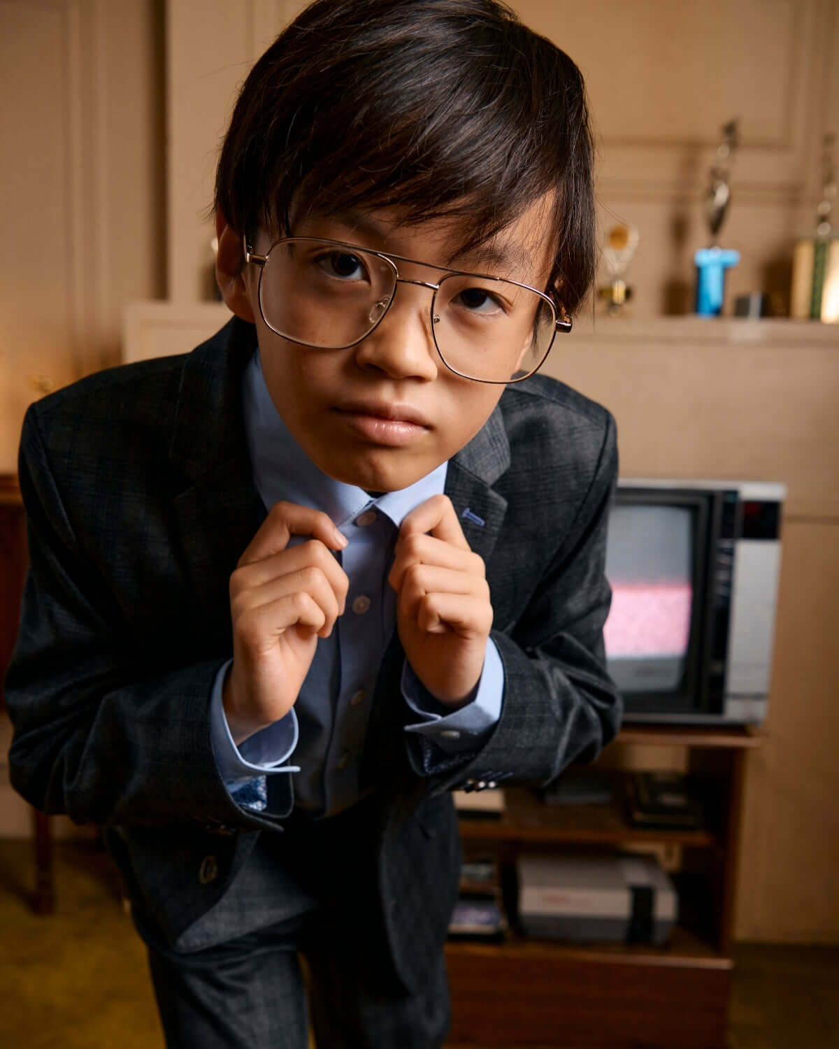 Stylish kid in a trendy grey plaid mod suit, showcasing confidence with oversized glasses and playful charm.