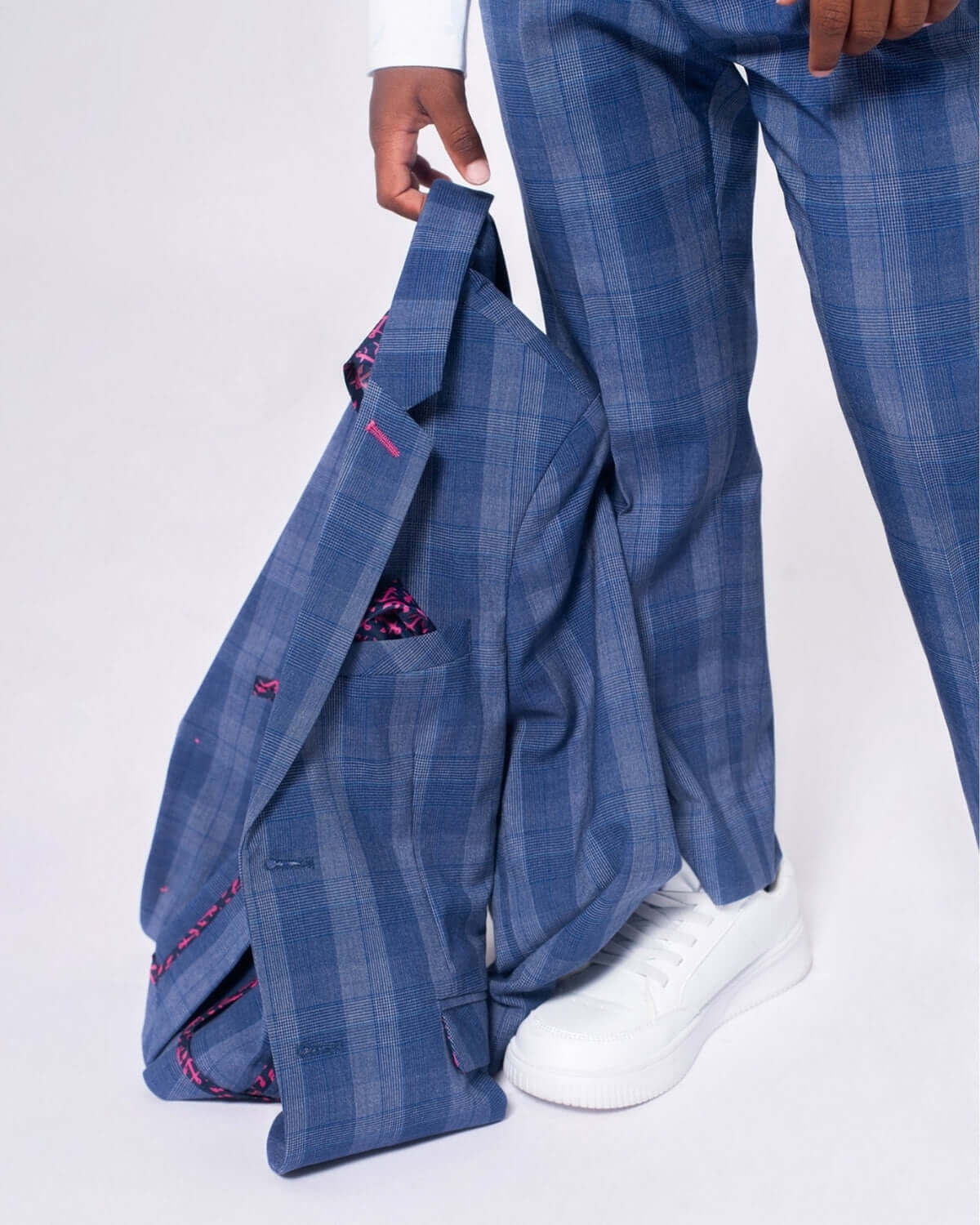 Chic boy in Indigo Glen Plaid suit, stylishly holding blazer, paired with fresh white sneakers for a trendy look.