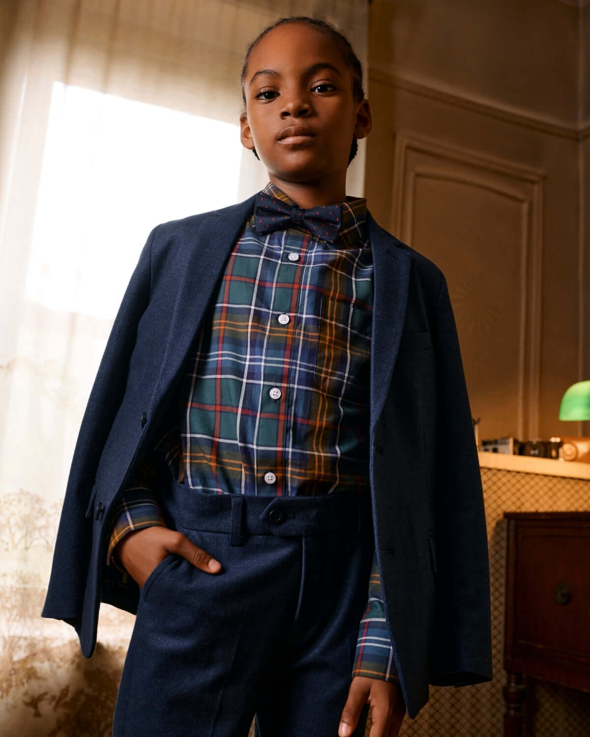 Stylish young model in navy suit with plaid shirt and bow tie, showcasing trendy kids clothes that's perfect for back to school.