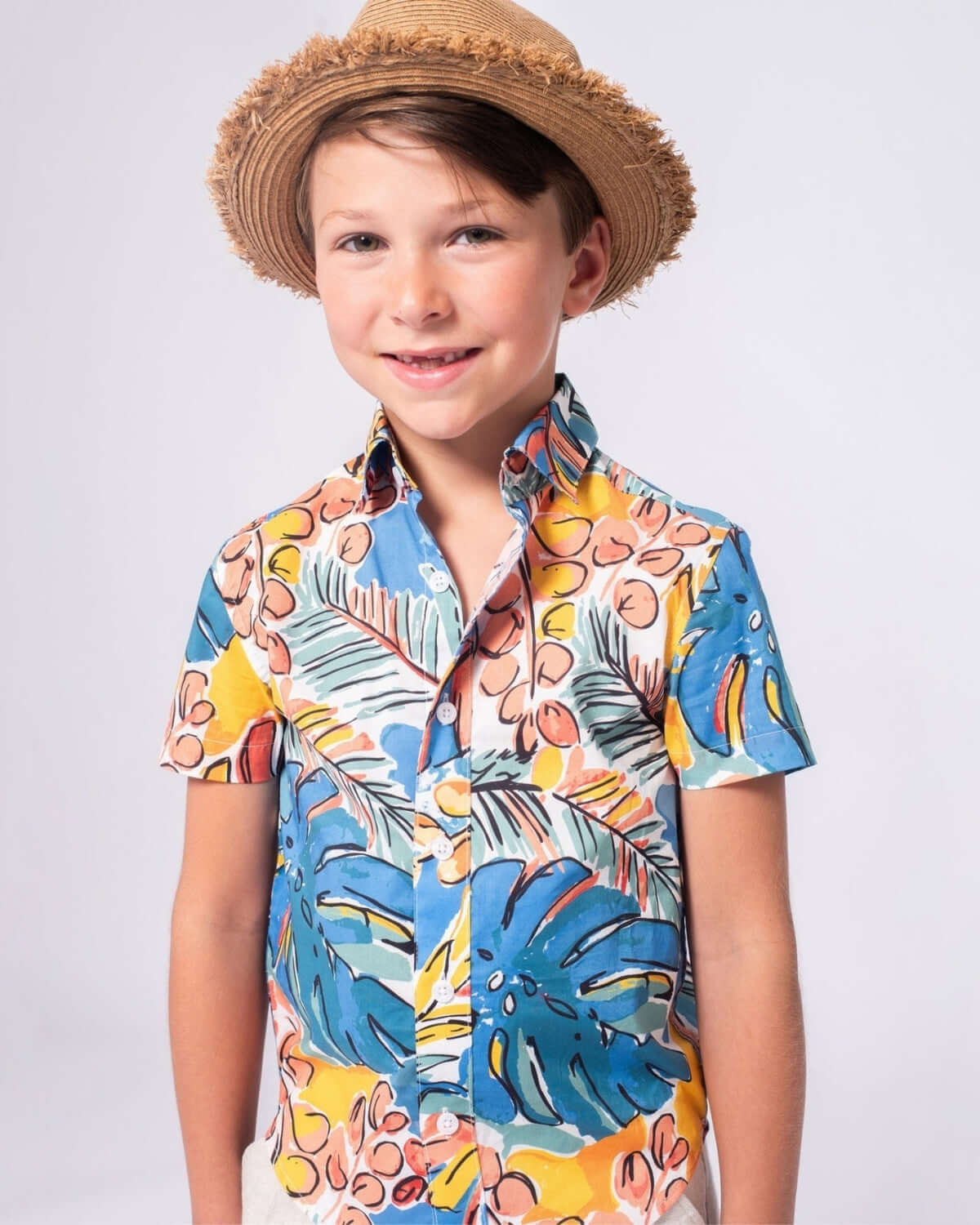 Stylish boy wearing Artist Flora Day Party Shirt with bright floral patterns and a straw hat, radiating summer vibes.