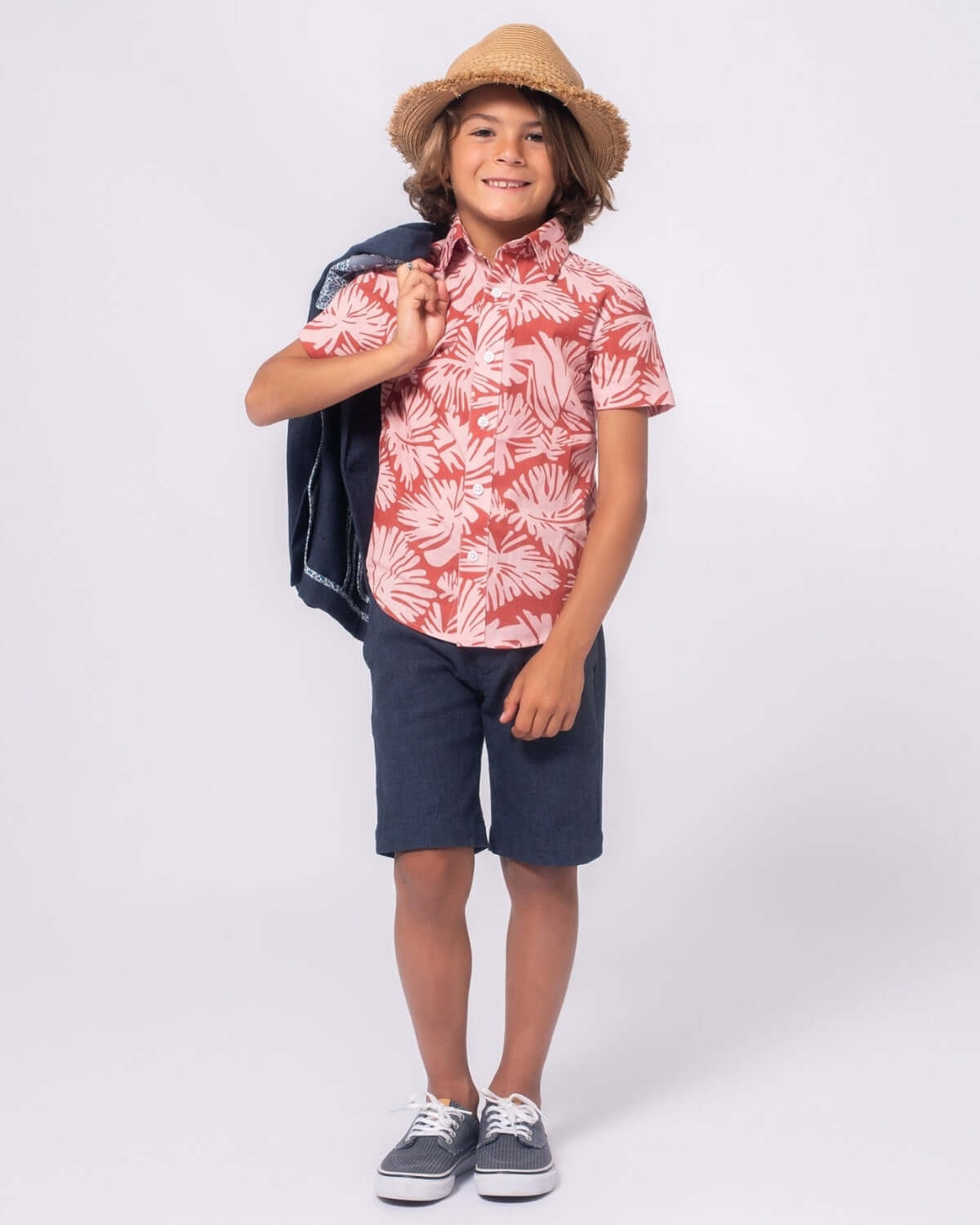 Boy wearing a Clay Garden Day Party Shirt, smiling with a straw hat and jacket on his shoulder.