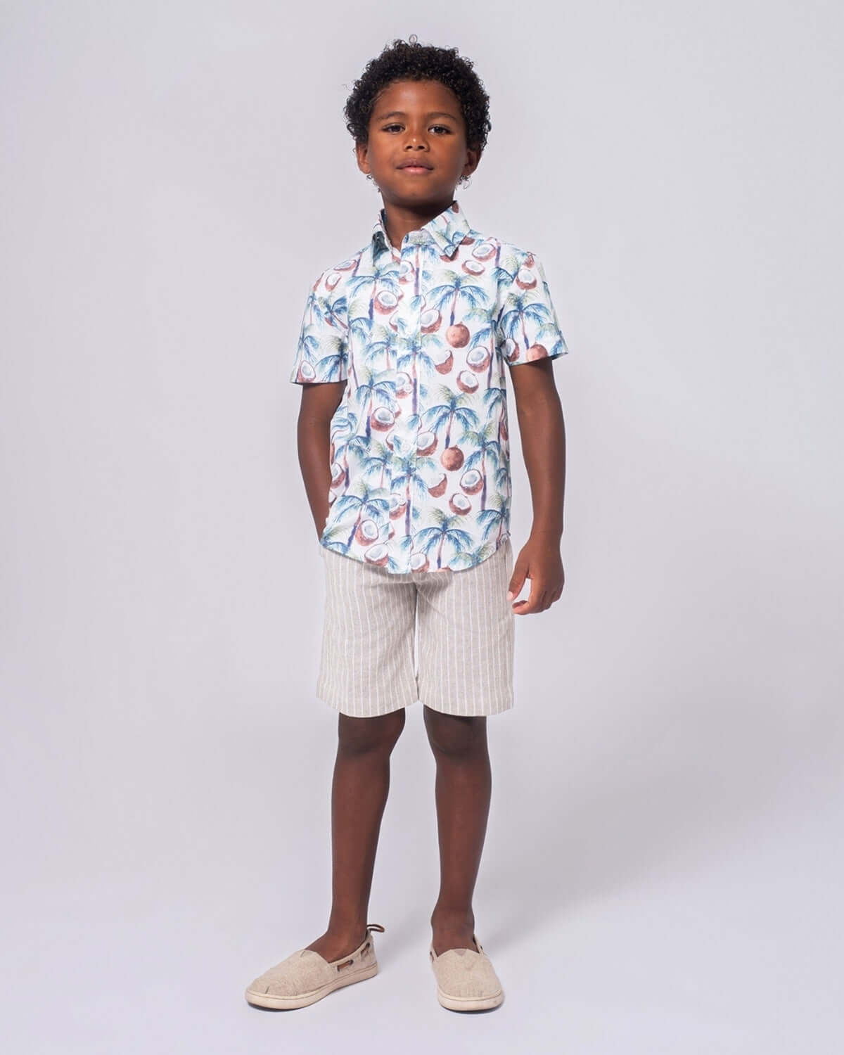 Boy wearing Coconut Palms Day Party Shirt with tropical design and shorts, ready for fun in the sun.