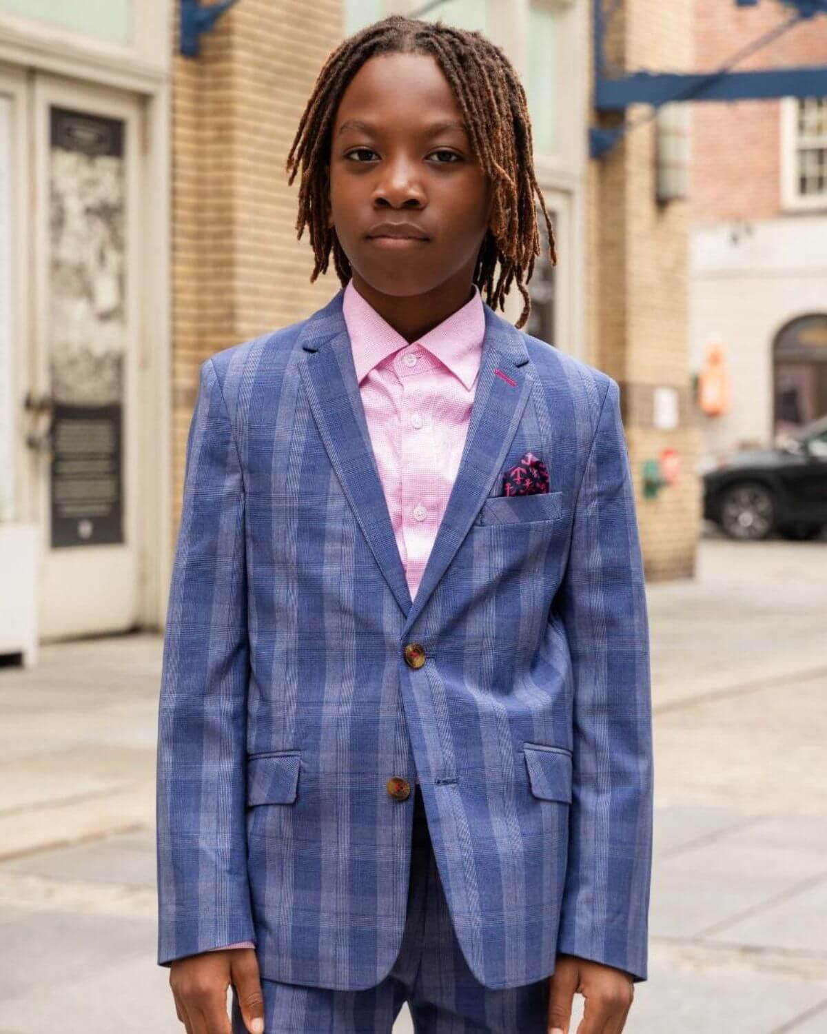 A child in a stylish blue suit with a Pink Standard Button Down Shirt, posing confidently in an urban setting.