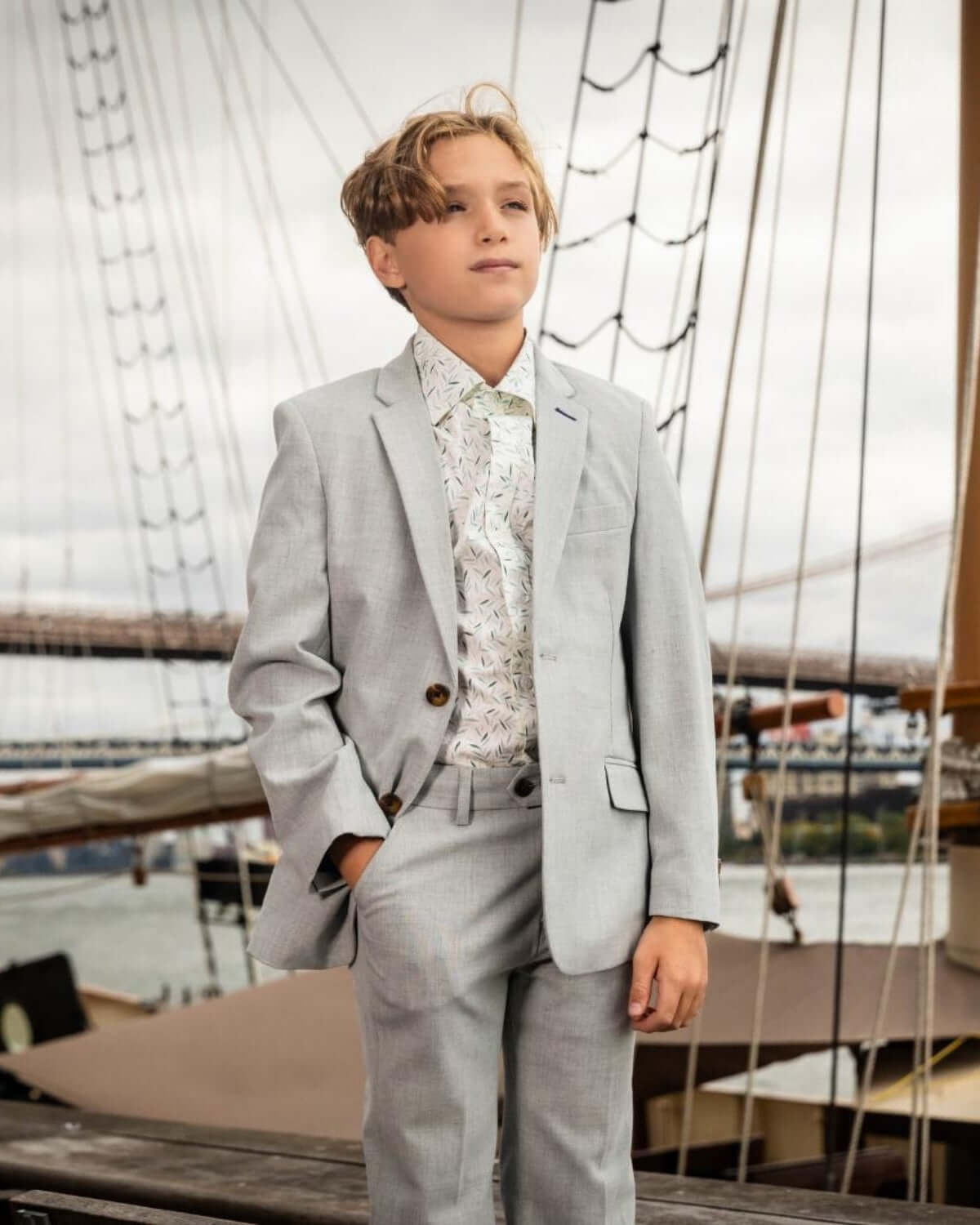 Stylish boy in a light grey suit with a vibrant Micro Greens shirt, ready for adventure by the dock.